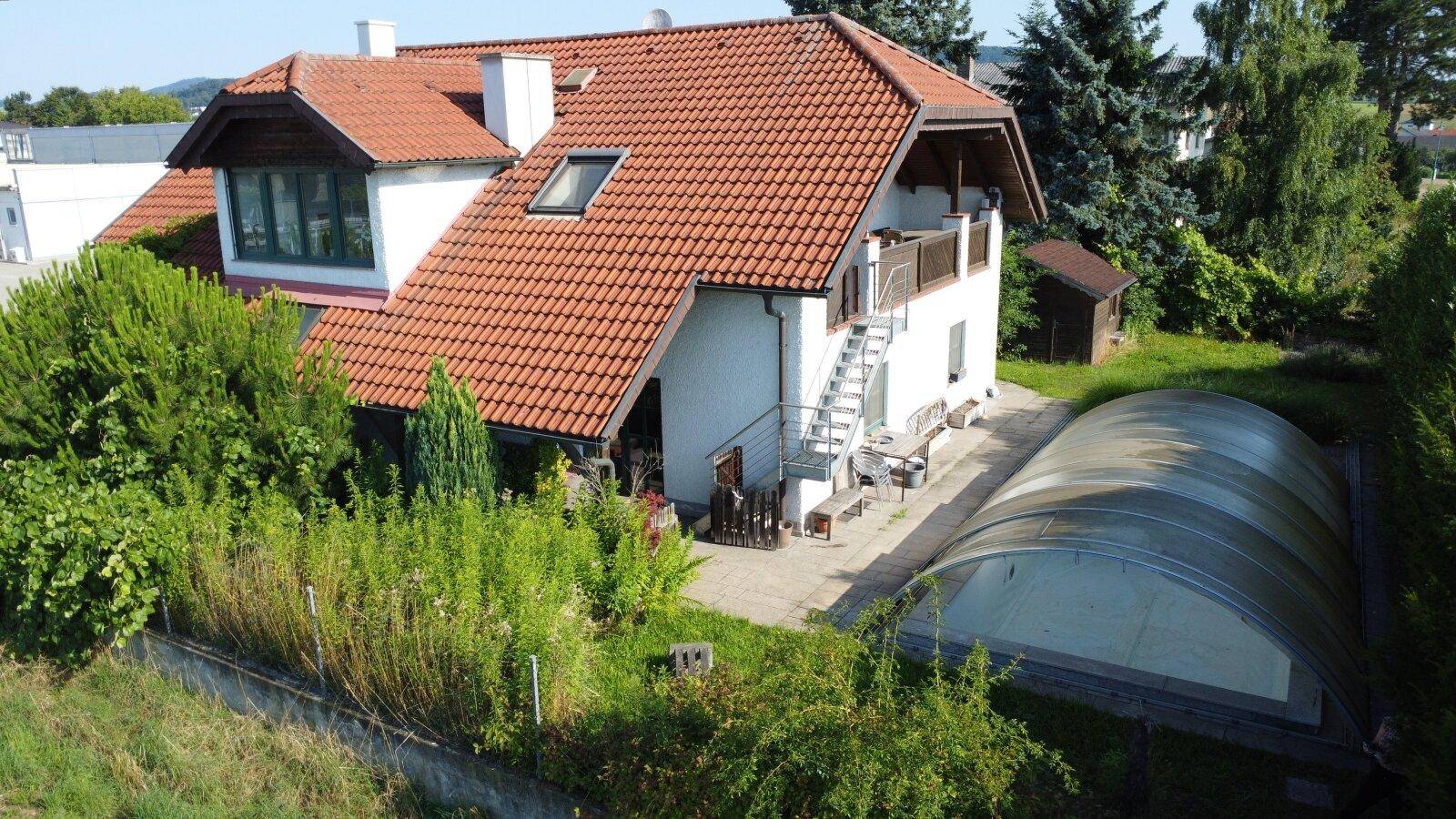 Luftaufnahme des Hauses mit großem Garten, überdachtem Pool und viel Grünfläche.