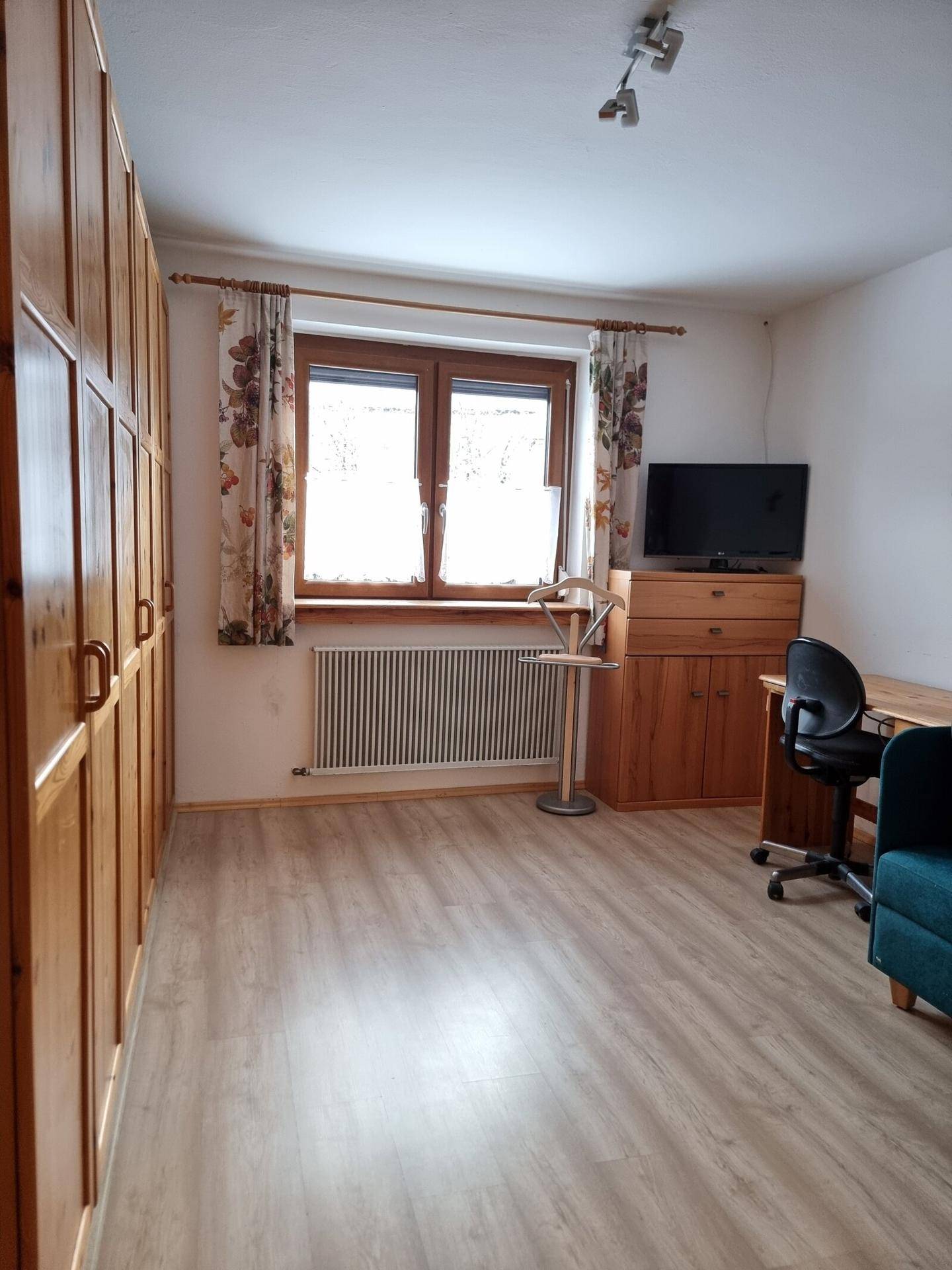 Helles Schlafzimmer mit Holzschränken, Laminatboden und Fenster.
