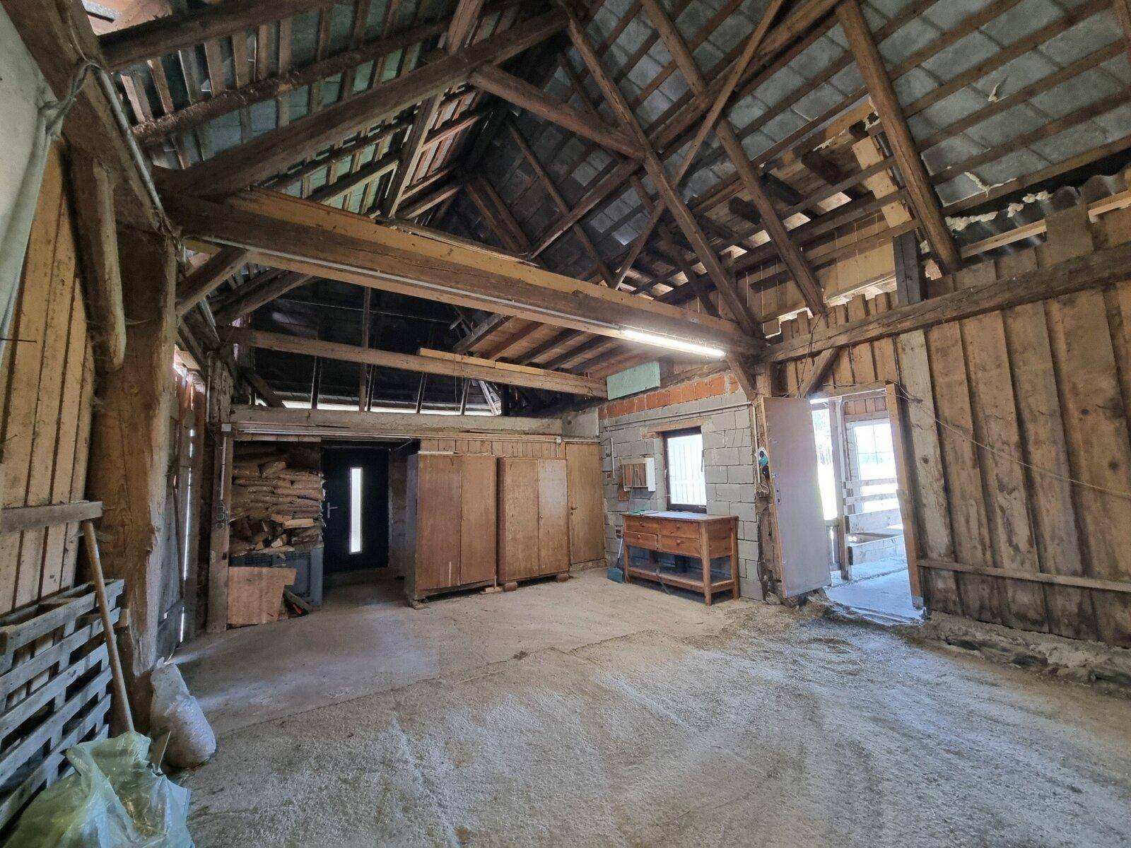 Innenansicht eines Scheunenbereichs mit sichtbarer Dachkonstruktion, Holzwänden und Betonblockelementen.