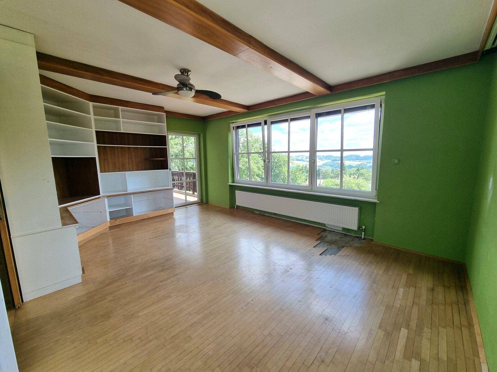 Geräumiges Wohnzimmer mit Holzbalken, Einbauregalen und großen Fenstern mit Weitblick.