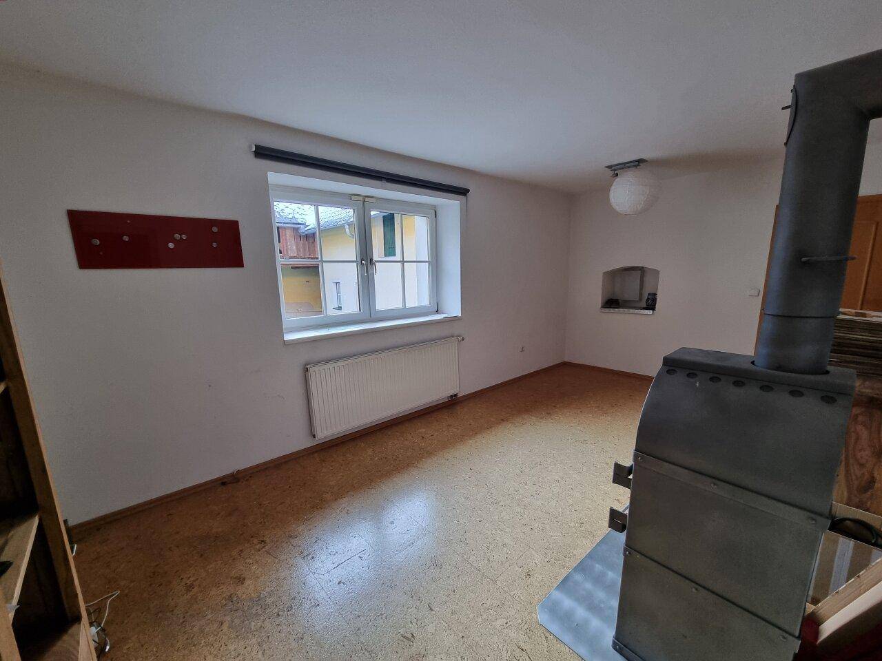 Heller Wohnraum mit Fenster, Heizkörper und einem markanten Holzofen als Wärmequelle.