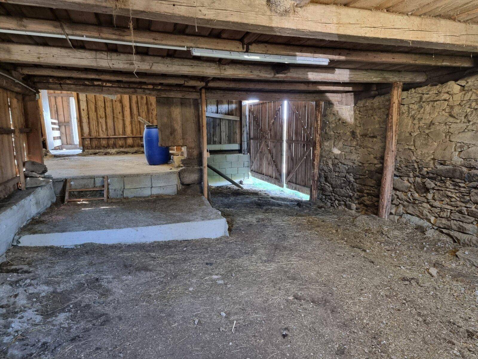Rustikaler Scheunenbereich mit Steinmauern, Holzbalken und einem offenen Tor.