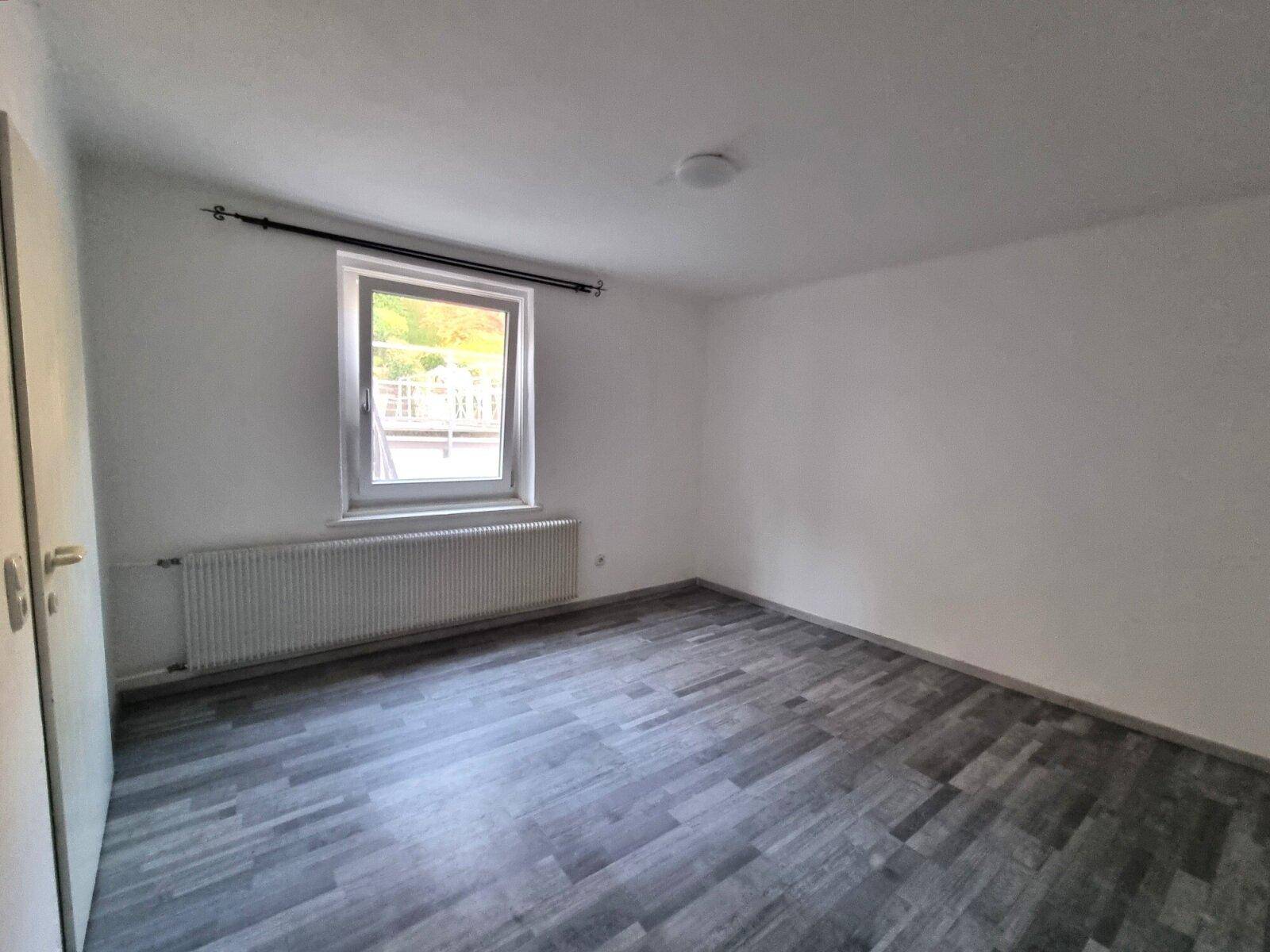 Leeres Schlafzimmer mit modernem grauem Laminatboden und einem Fenster.