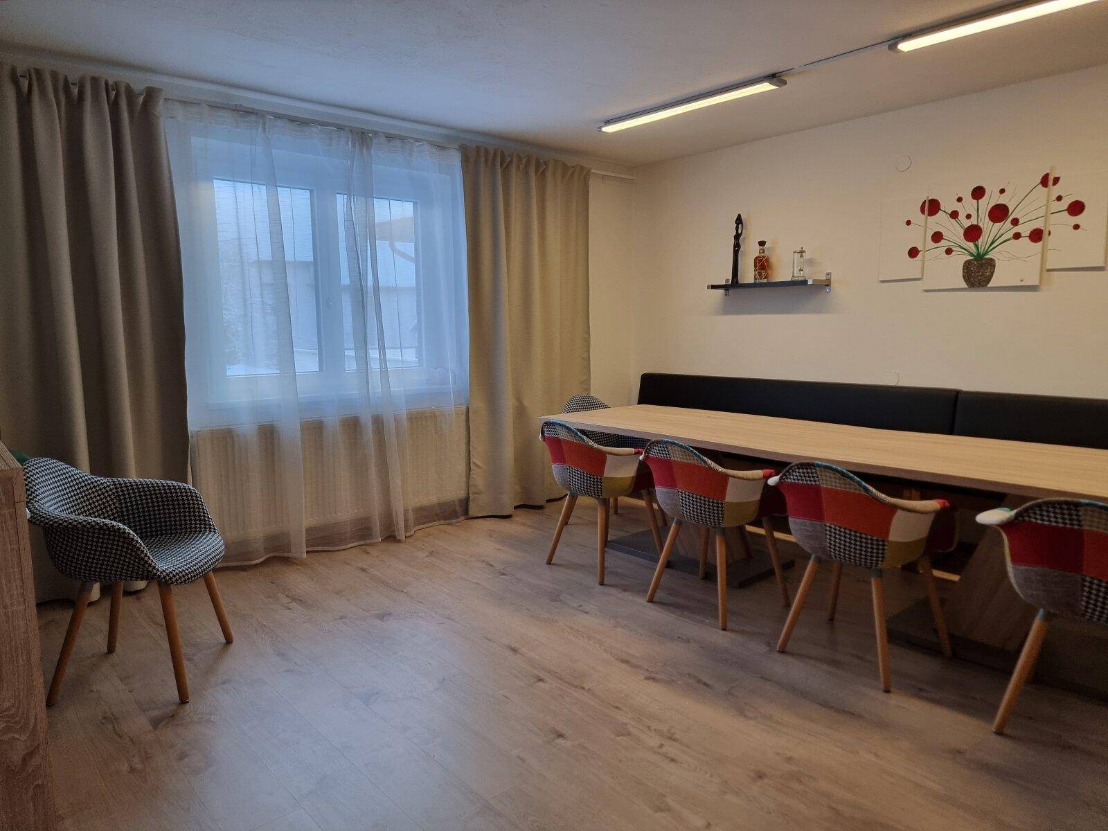 Geräumiger Essbereich mit langem Tisch, bunten Stühlen und Laminatboden.