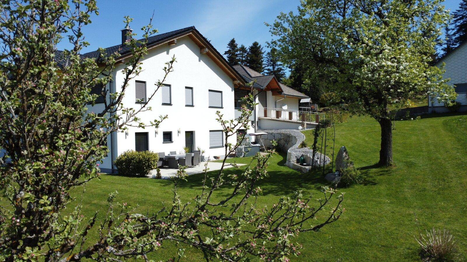 Sonniger Terrassenbereich mit Gartenmöbeln hinter dem Haus, umgeben von gepflegtem Rasen.