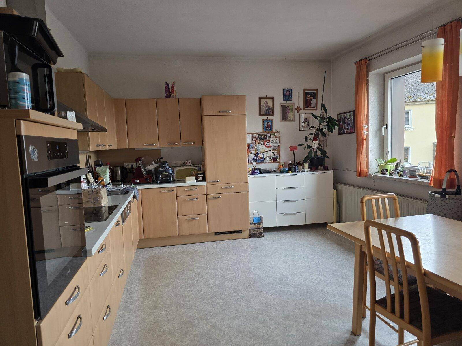 Geräumige Wohnküche mit Holzschränken, Essbereich und Fenster für Tageslicht.