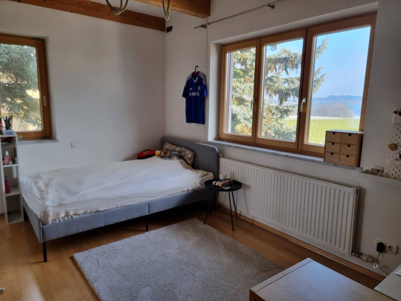 Helles Schlafzimmer mit Holzboden, großen Fenstern und weitem Blick ins Grüne.
