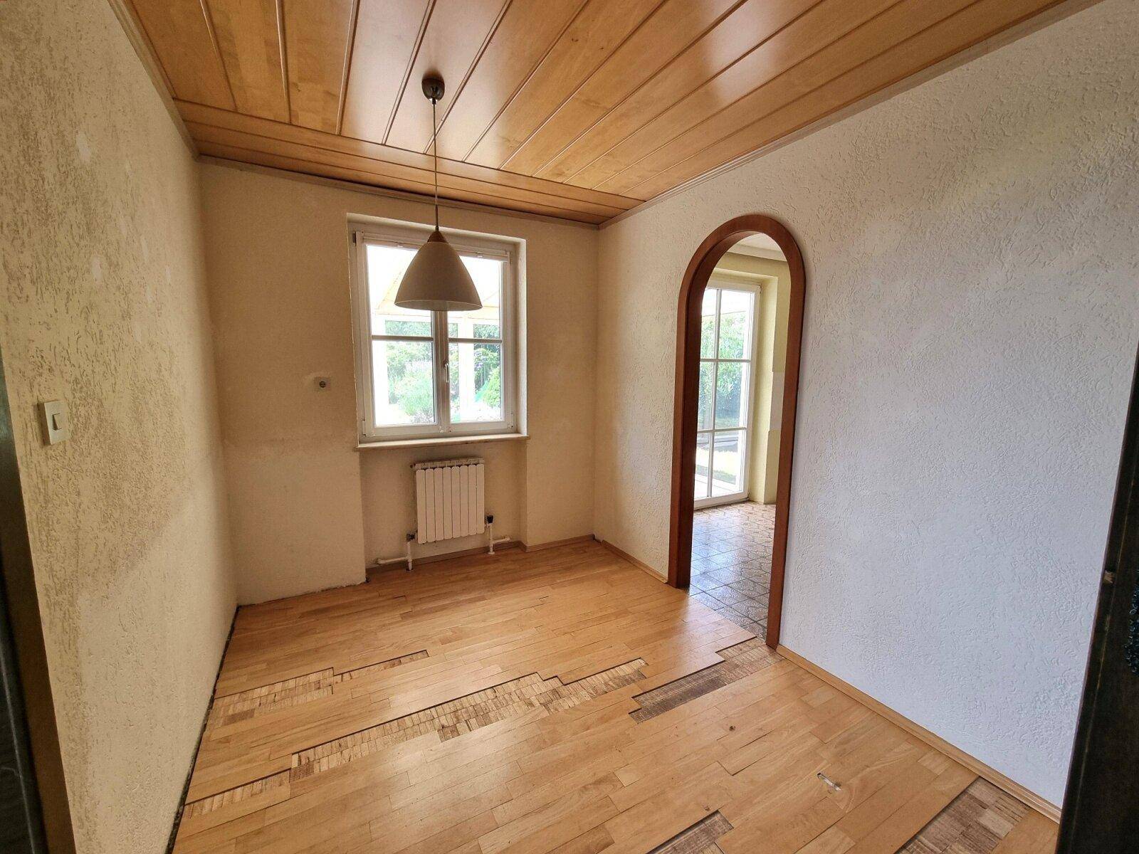 Esszimmer mit Holzboden, Holzdecke und einem Fenster, verbunden durch einen Rundbogen.