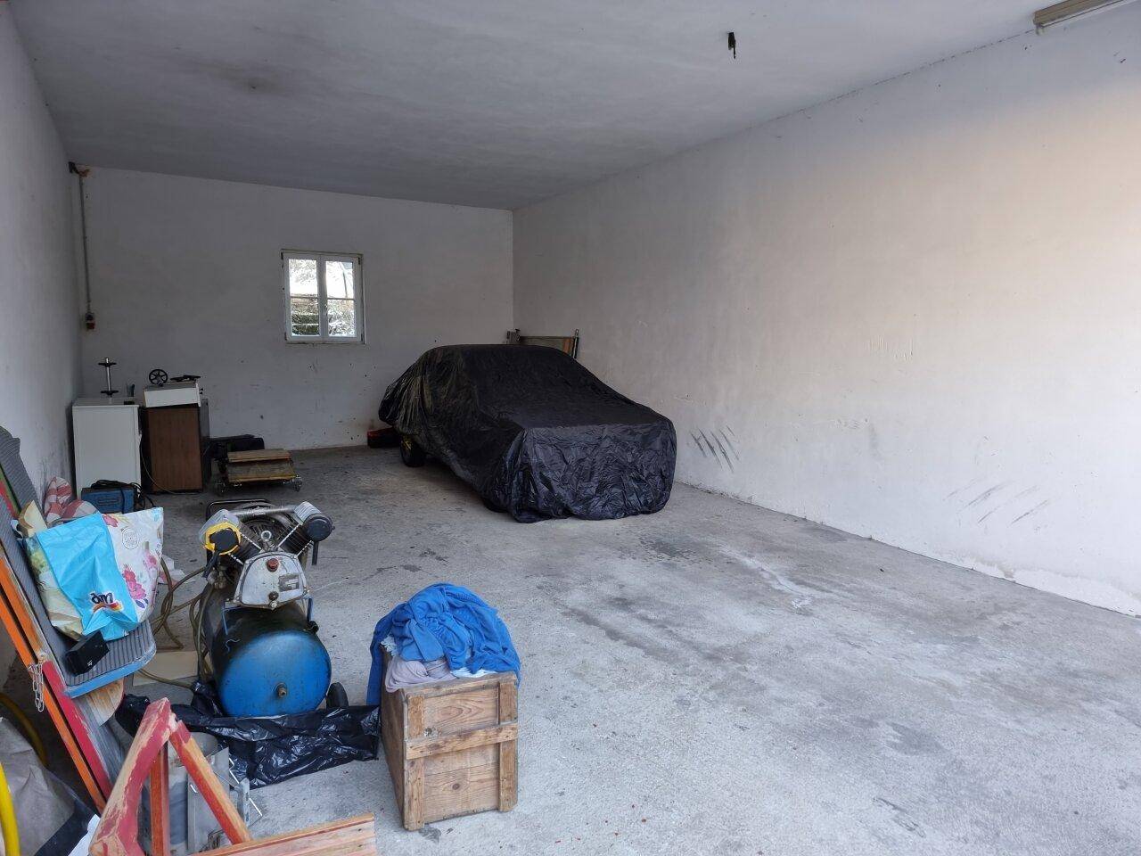 Geräumige Garage mit Betonboden, Fenster und einem abgedeckten Fahrzeug.
