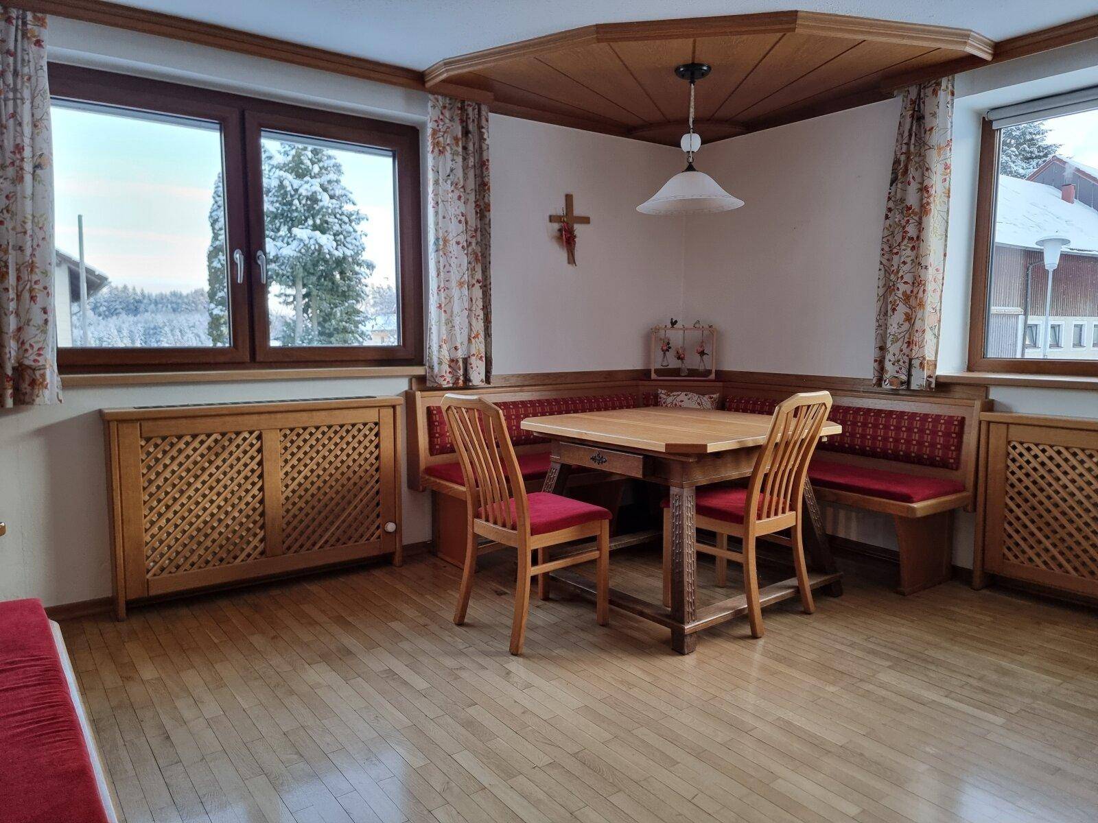 Gemütliche Essecke mit Holztisch, Eckbank und Blick auf die verschneite Landschaft.