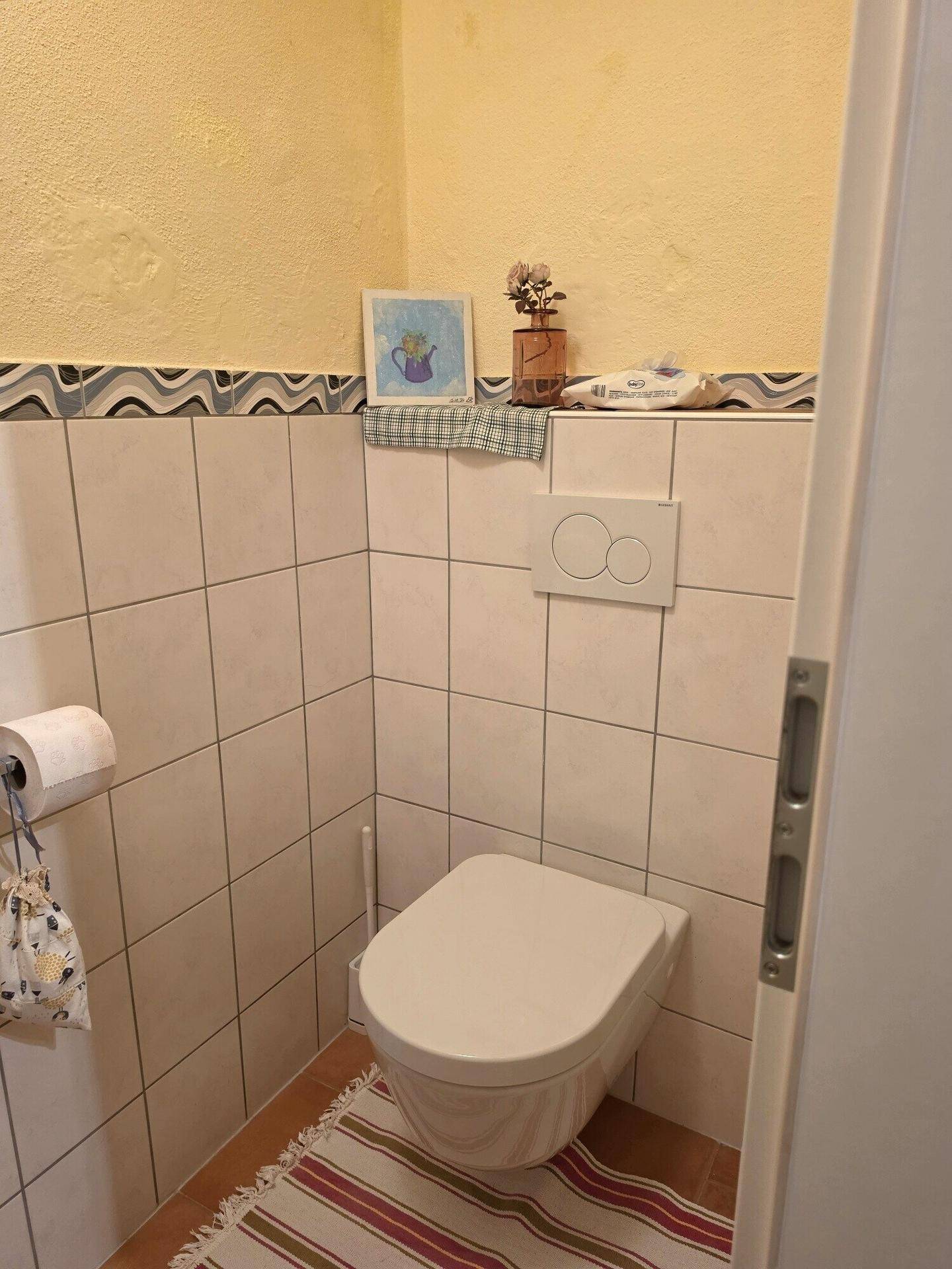 Separates WC mit Wand-WC und hellen Fliesen, praktisch und sauber.