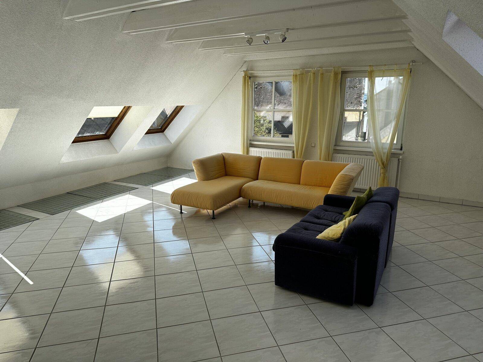 Helles Wohnzimmer im Dachgeschoss mit schrägen Decken, Dachfenstern und Fliesenboden.