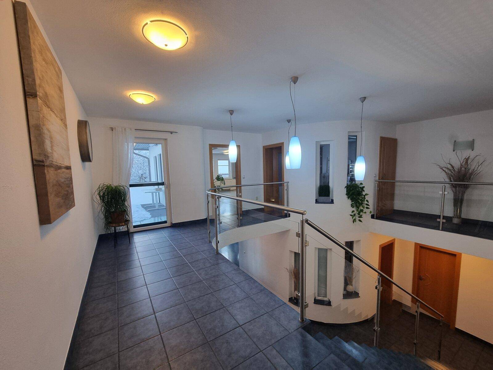 Geräumiger Eingangsbereich mit moderner Glasbrüstung, Treppe und dunklen Fliesen.