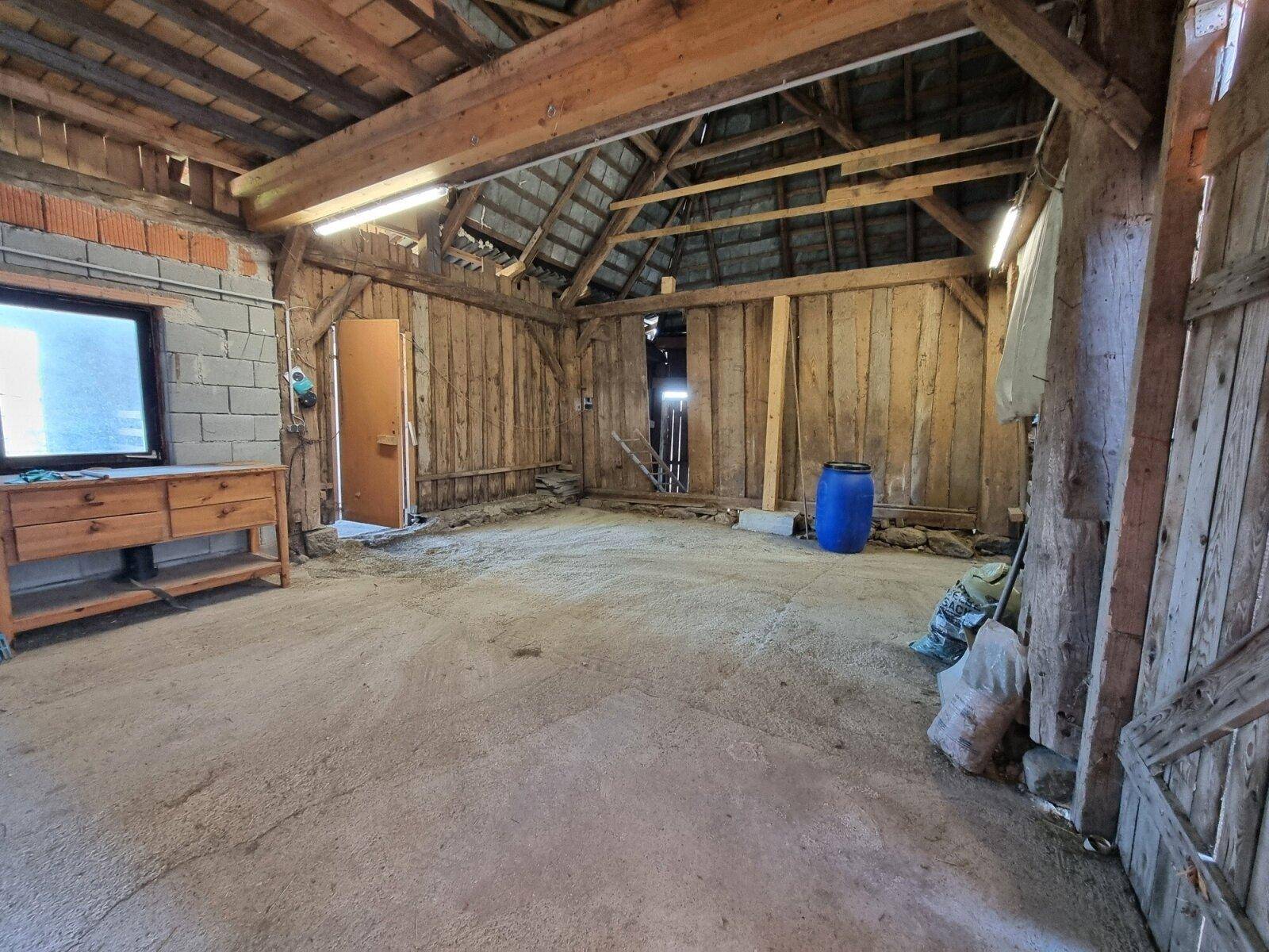 Geräumiger Scheunen- oder Lagerbereich mit Holzwänden, sichtbarer Dachkonstruktion und Betonboden.