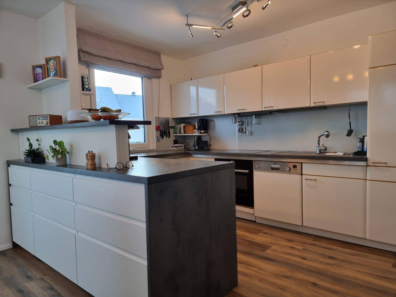 Moderne Küche mit weißen Hochglanzfronten, dunkler Arbeitsplatte und Holzboden.