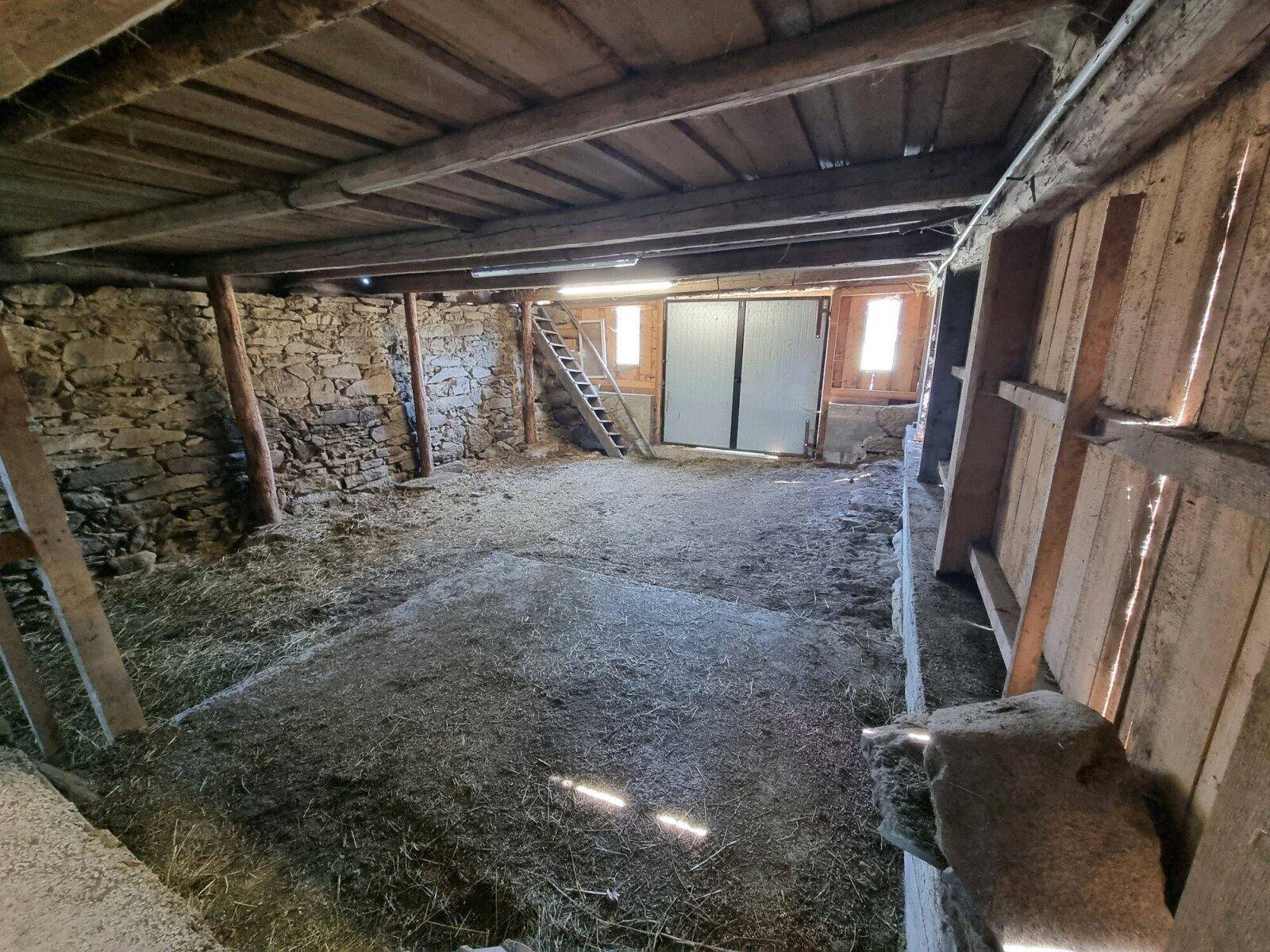 Großer Scheunenbereich mit Steinmauern, Holzbalken und einer breiten Schiebetür.