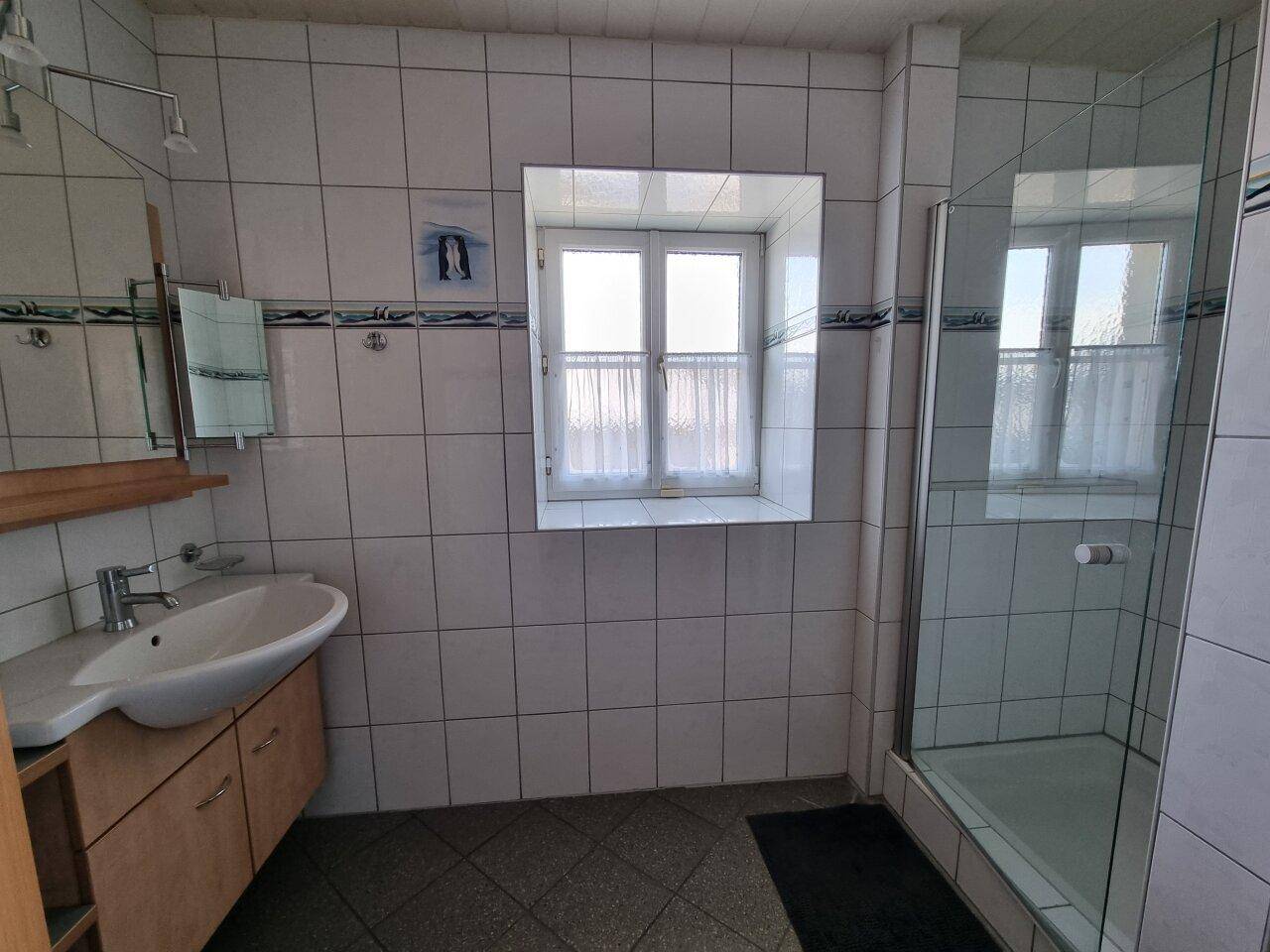 Gefliestes Badezimmer mit Dusche, Waschbecken und Fenster für Tageslicht.