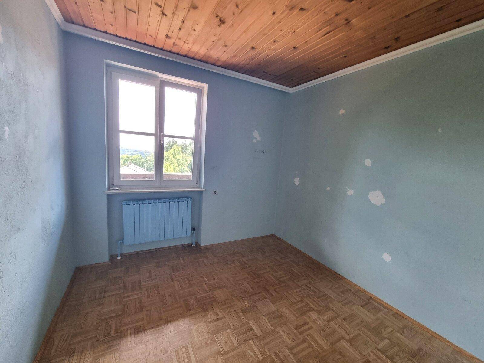 Schlafzimmer mit blauen Wänden, Holzbalkendecke und Parkettboden, renovierungsbedürftig.