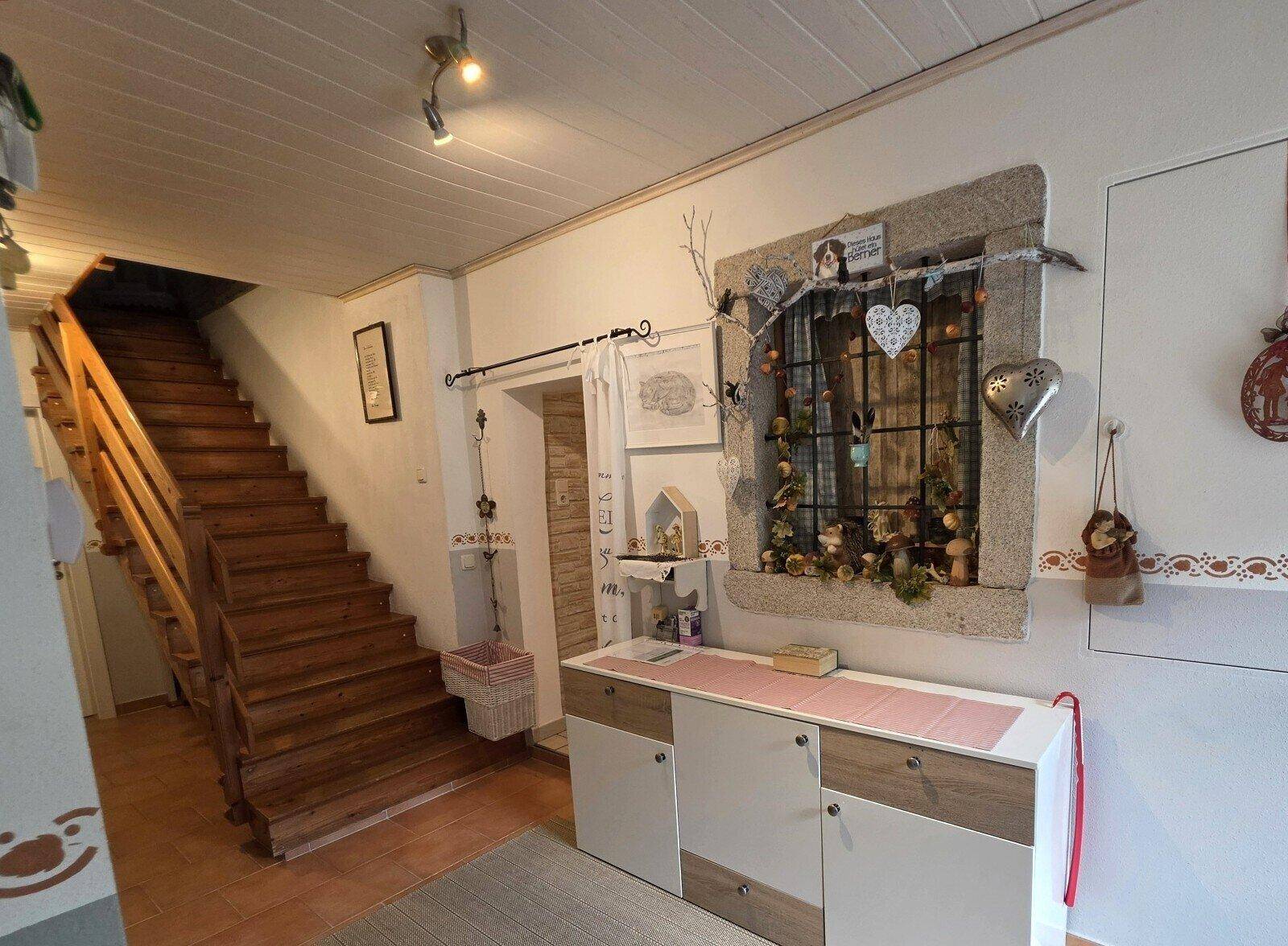 Flur mit rustikaler Holztreppe, Terrakottaboden und einem dekorativen Fenster.