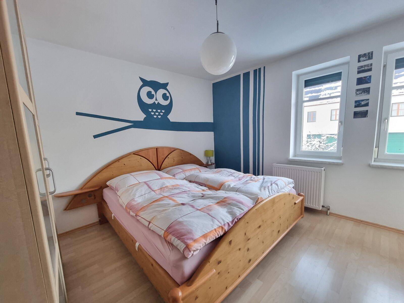 Helles Schlafzimmer mit Holzbett, Laminatboden und verspielter Eulen-Wanddekoration.