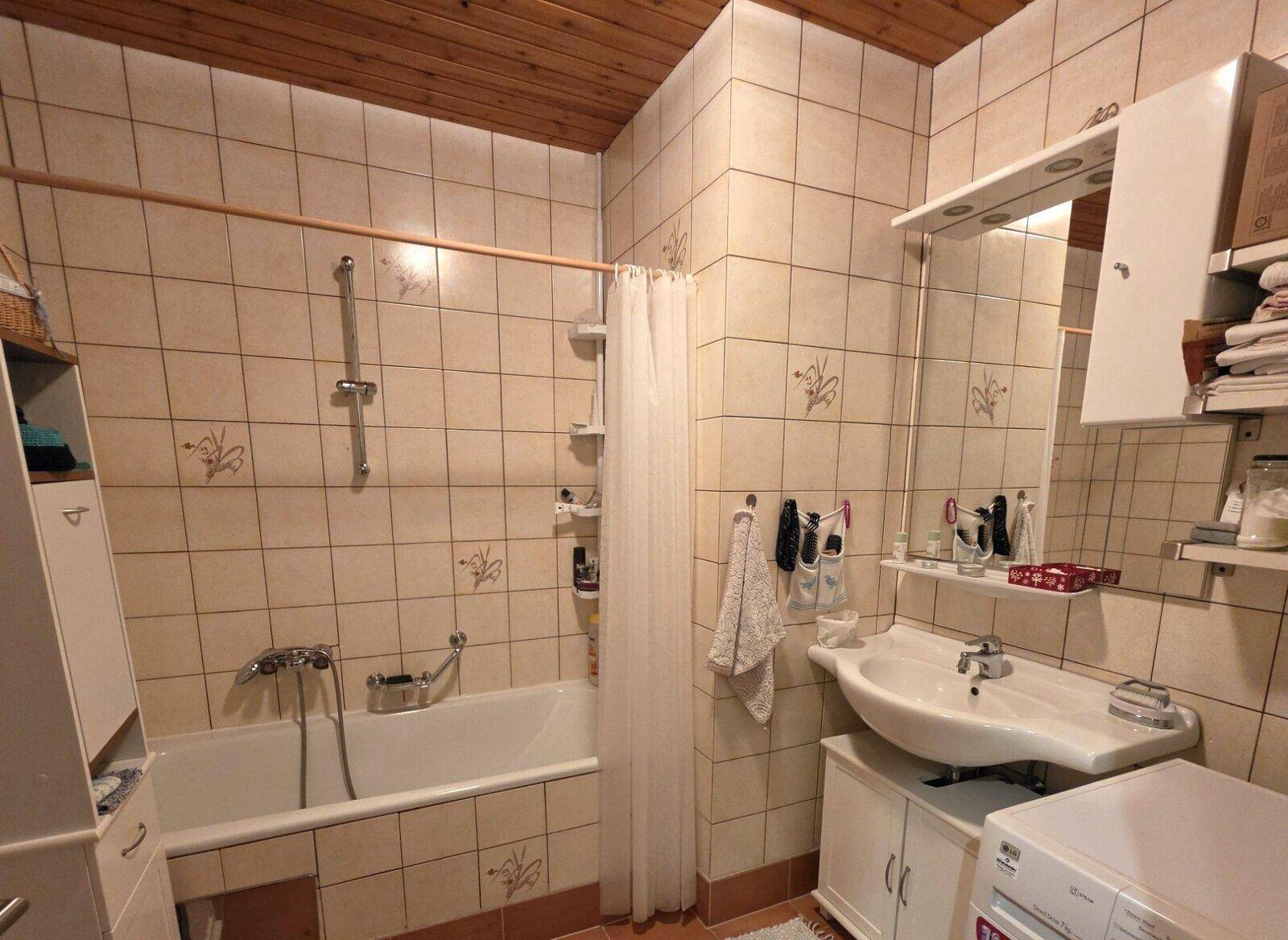 Badezimmer mit Badewanne, Waschbecken und hellen Fliesen, funktional eingerichtet.