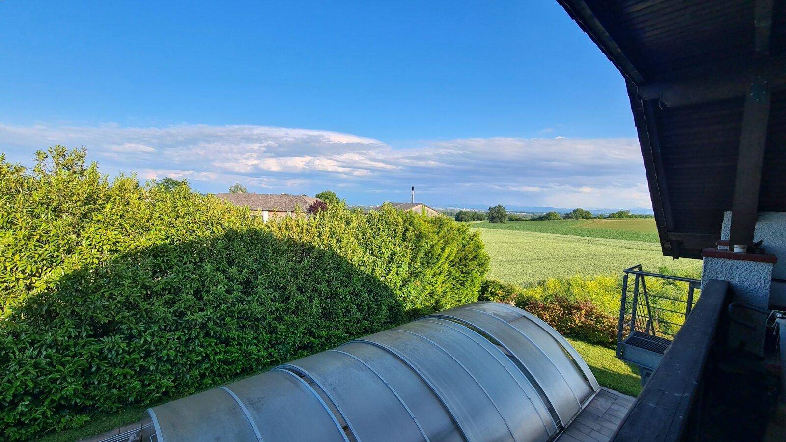 Blick von einem Balkon auf den überdachten Poolbereich und die weite grüne Landschaft.