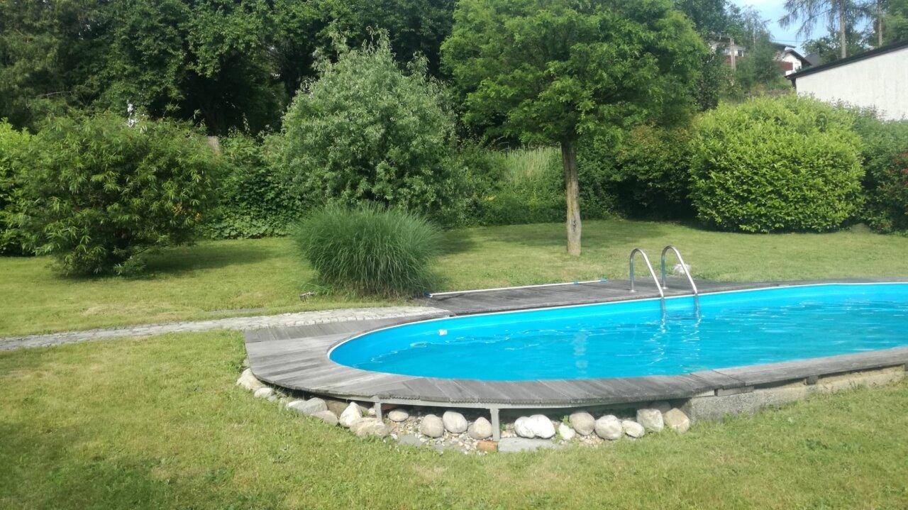Großer Garten mit ovalem Pool und umgebender Rasenfläche sowie Bäumen.
