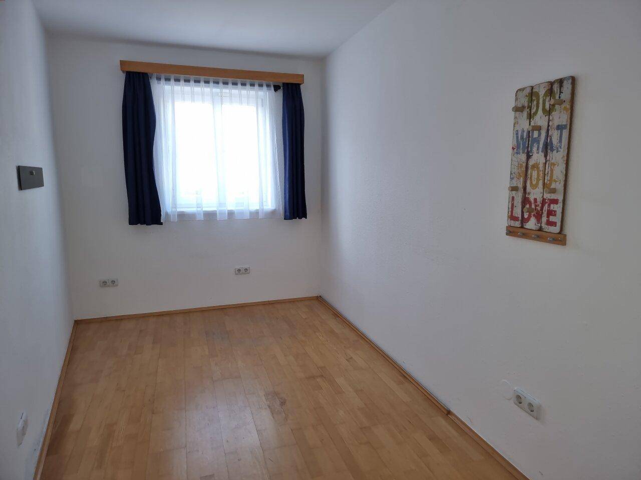 Kleines Schlafzimmer mit Holzboden, hellem Fenster und schlichter Wandgestaltung.
