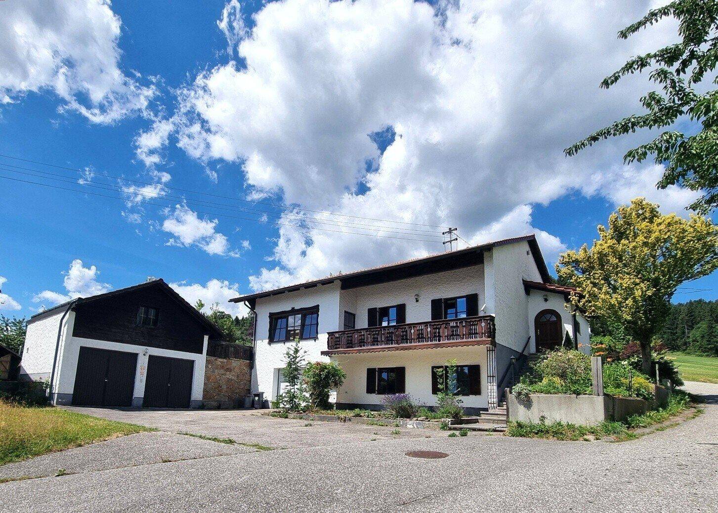 Einfamilienhaus mit Doppelgarage und Balkon, umgeben von ländlicher Natur unter blauem Himmel.