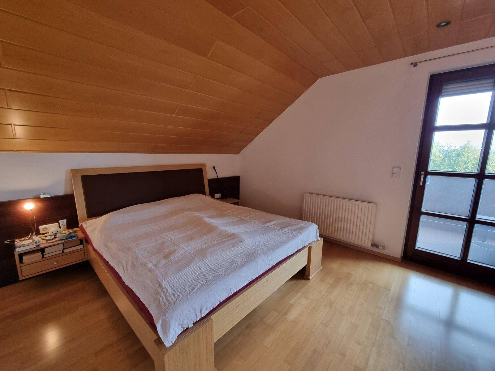 Schlafzimmer im Dachgeschoss mit Holzdecken, Doppelbett und Zugang zu einem Außenbereich.