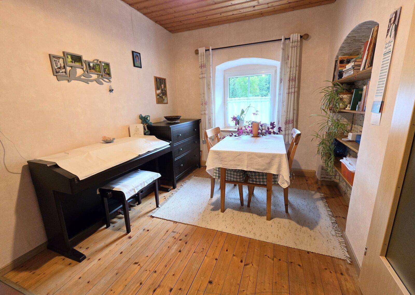 Essbereich oder Arbeitszimmer mit Holzboden, Esstisch und einem Fenster mit Blick ins Grüne.
