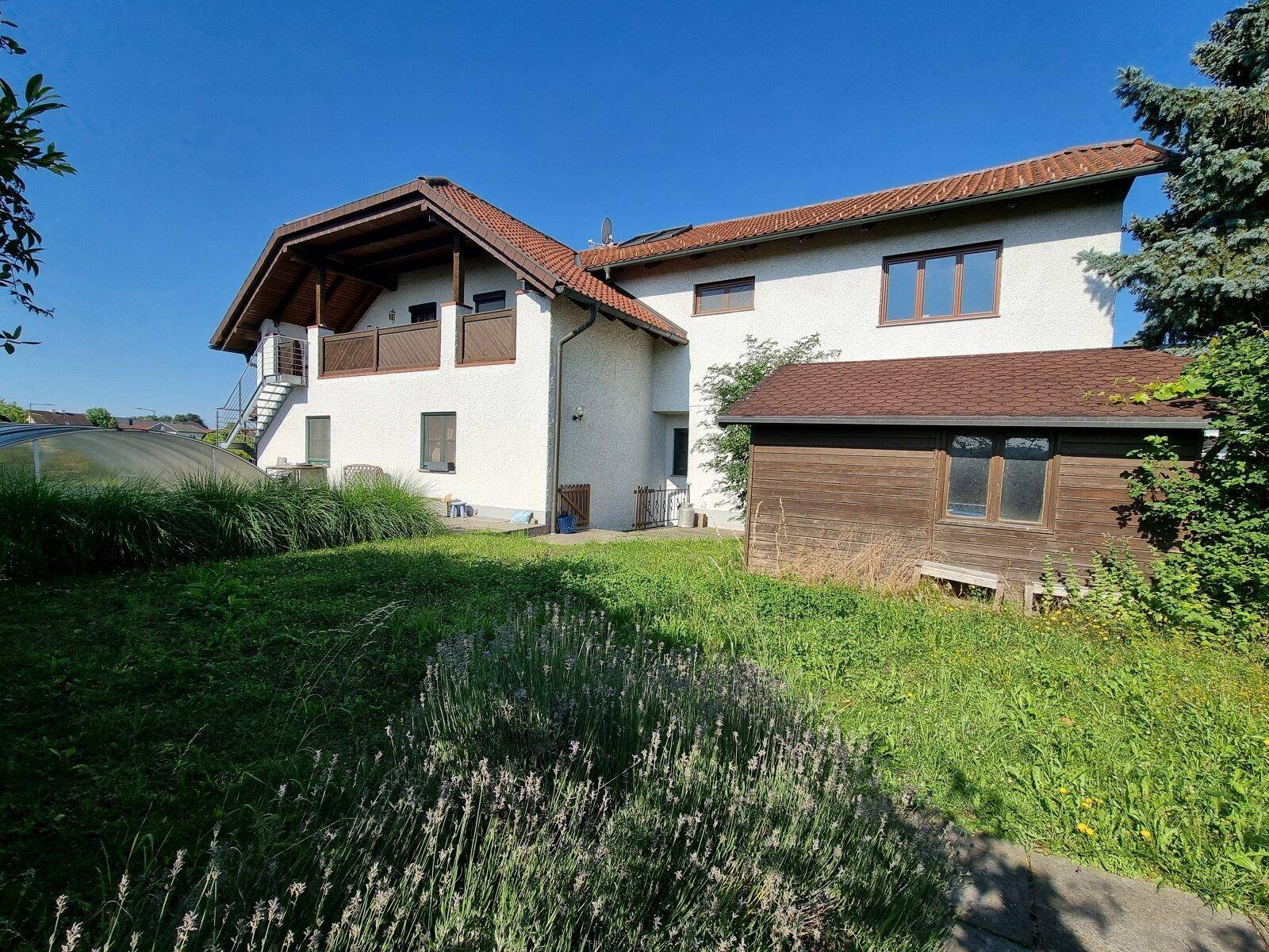 Rückansicht des Hauses mit großem, gepflegten Garten, Rasenfläche und einem kleinen Holzschuppen.