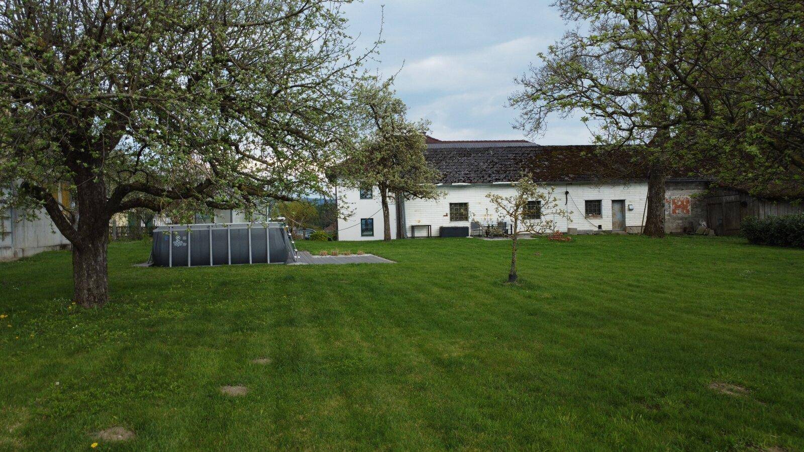 Weitläufiger Garten mit grüner Rasenfläche, alten Bäumen und einem Aufstellpool.