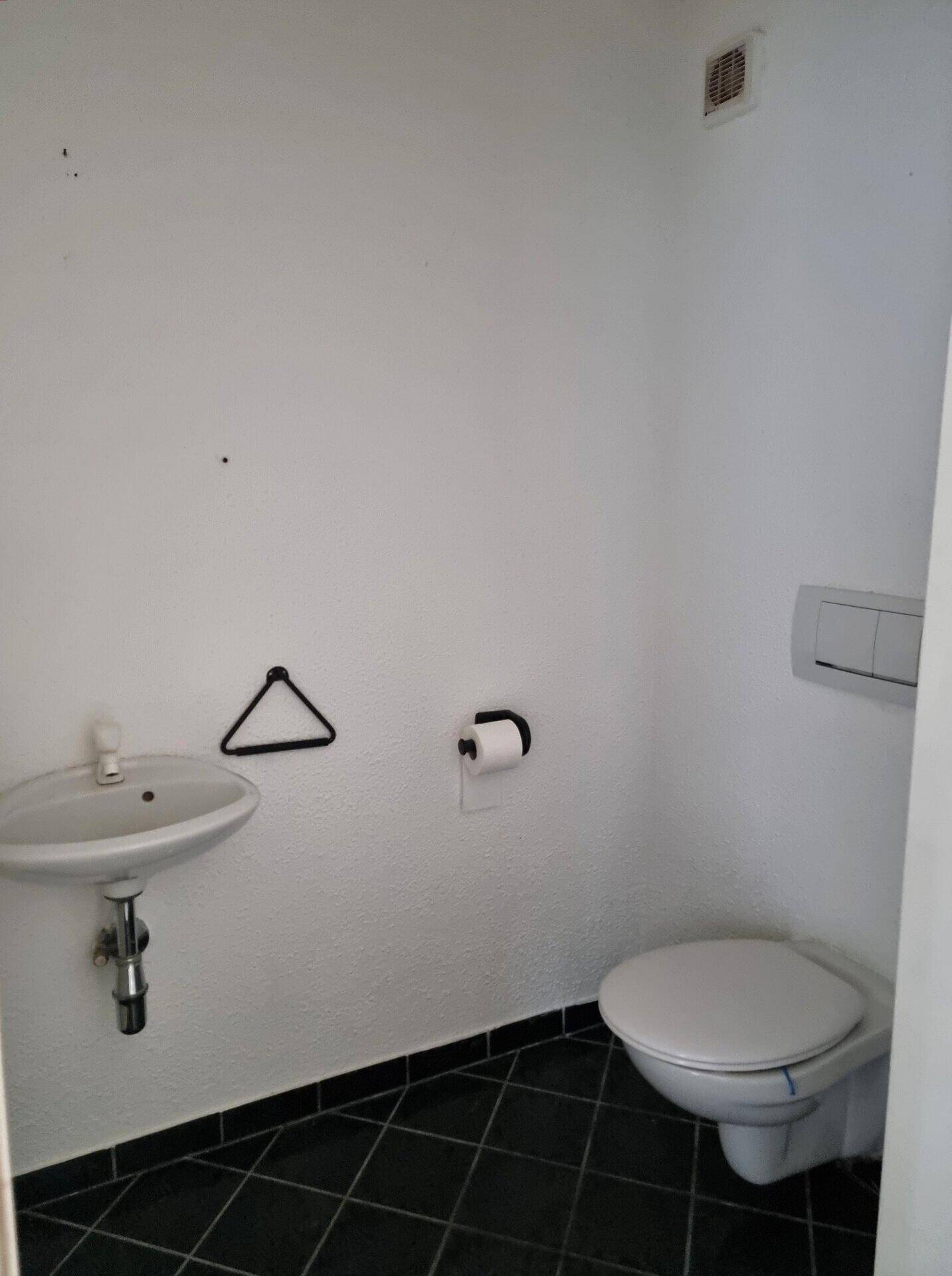 Kleines Gäste-WC mit wandhängender Toilette, Waschbecken und dunklem Fliesenboden.