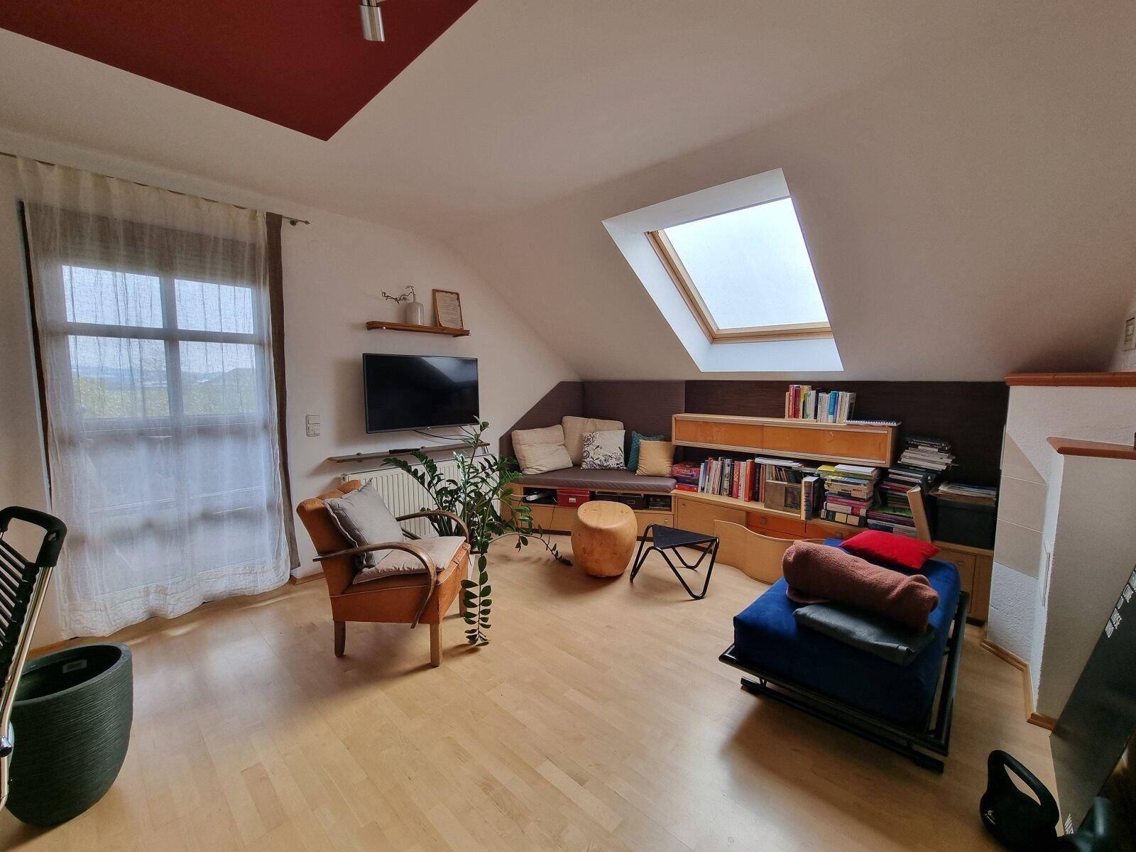 Gemütlicher Wohnbereich im Dachgeschoss mit schrägen Decken, Dachfenster und Blick ins Grüne.