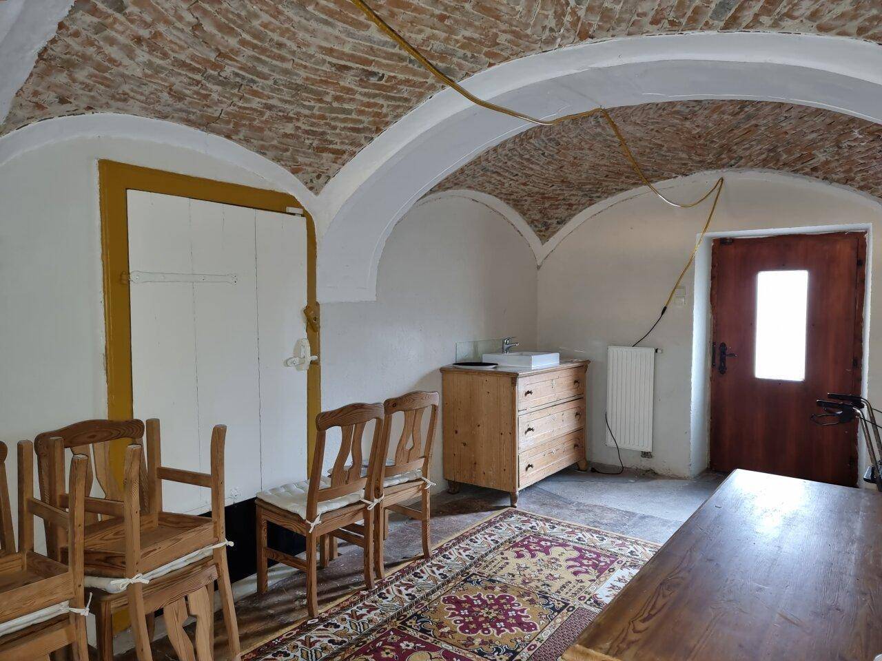 Rustikaler Kellerraum mit Ziegelgewölbedecke, Holztisch und Stühlen.