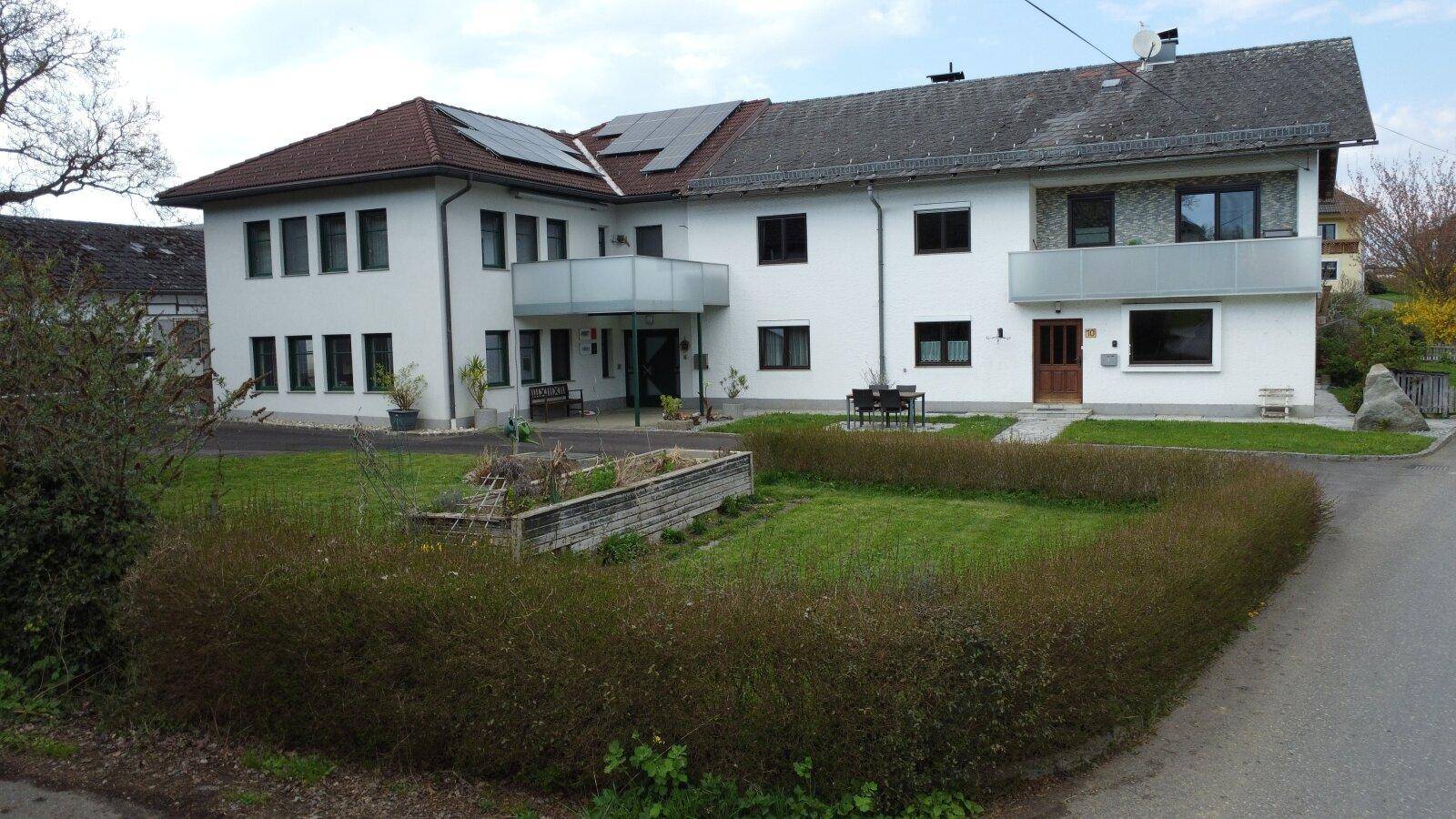 Wohnhausfassade mit Balkonen, Photovoltaikanlage und einem gepflegten Vorgarten mit Hecke.