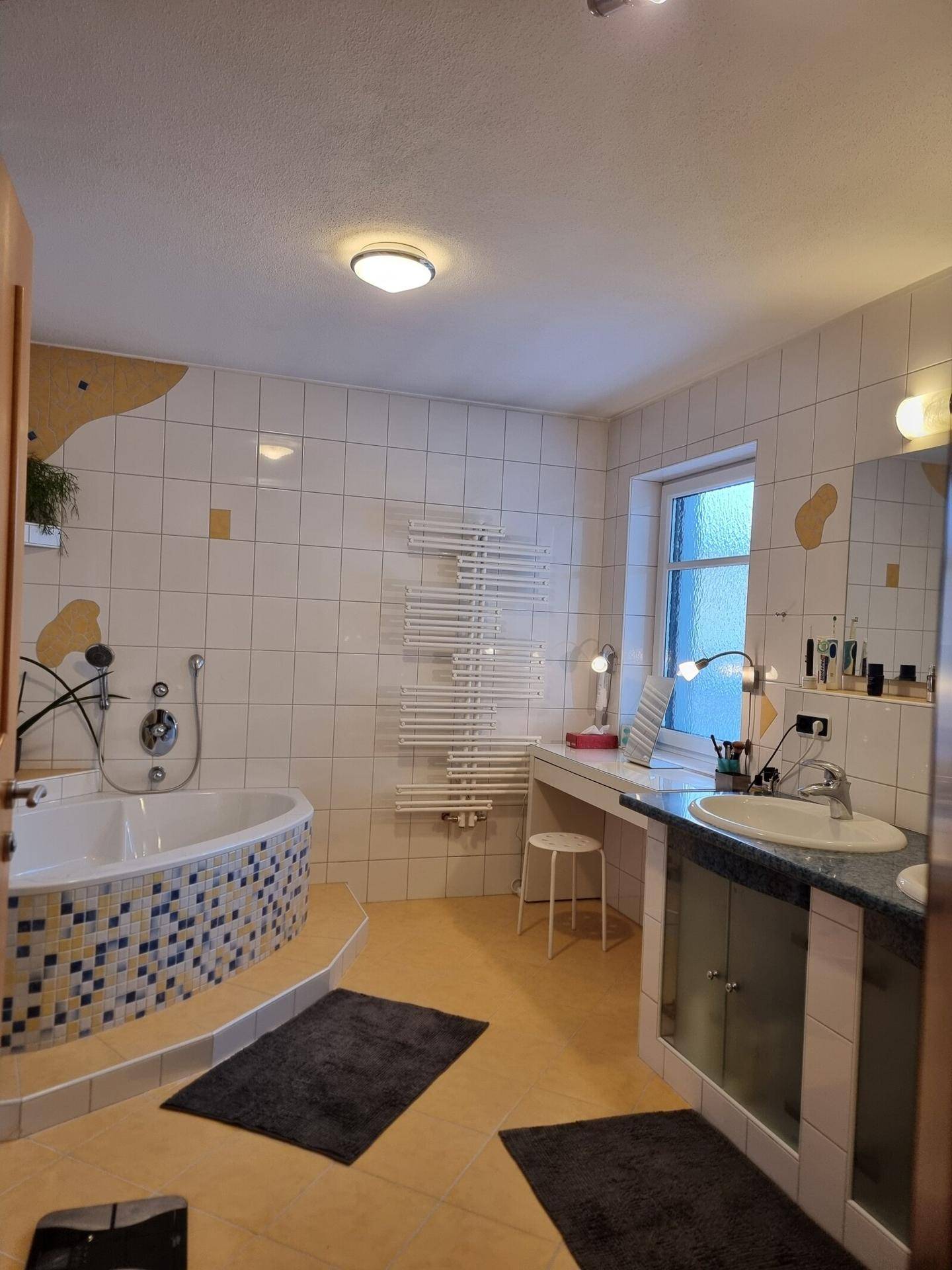Helles Badezimmer mit Eckbadewanne, weißen Fliesen und beheiztem Handtuchhalter.