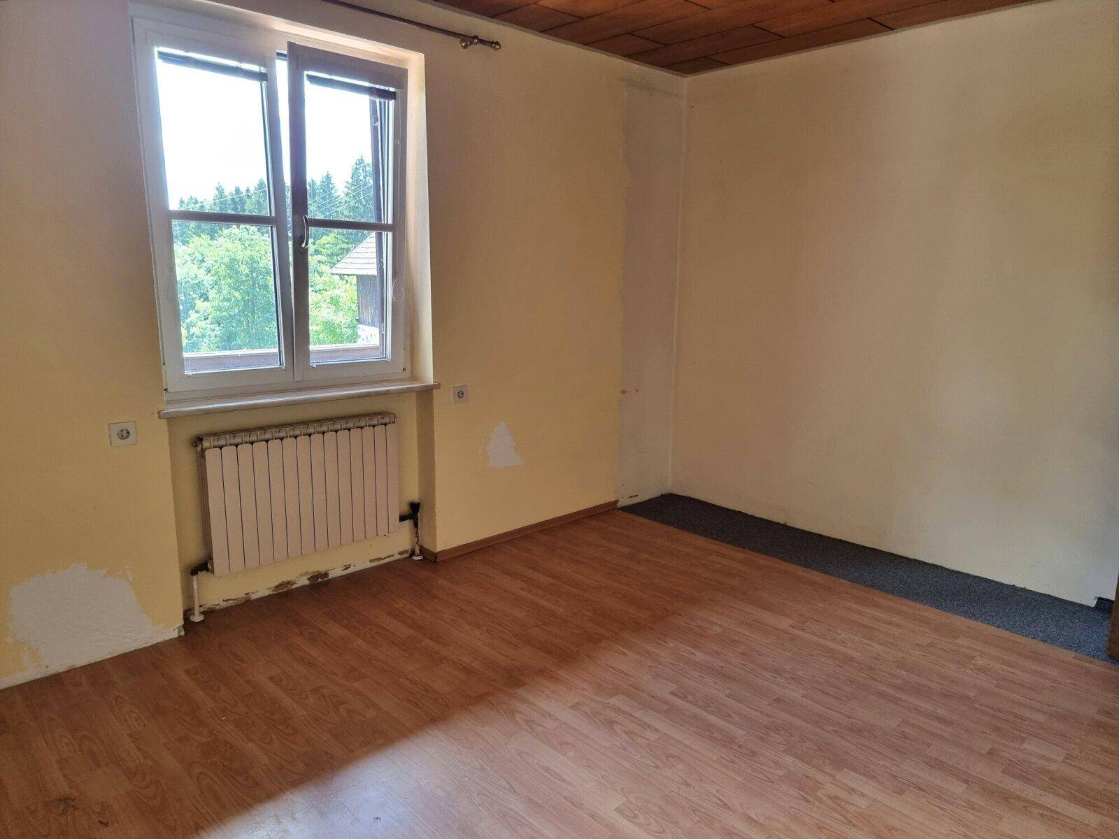 Helles Schlafzimmer mit Holzboden, Holzdecke und einem Fenster mit Blick ins Grüne.
