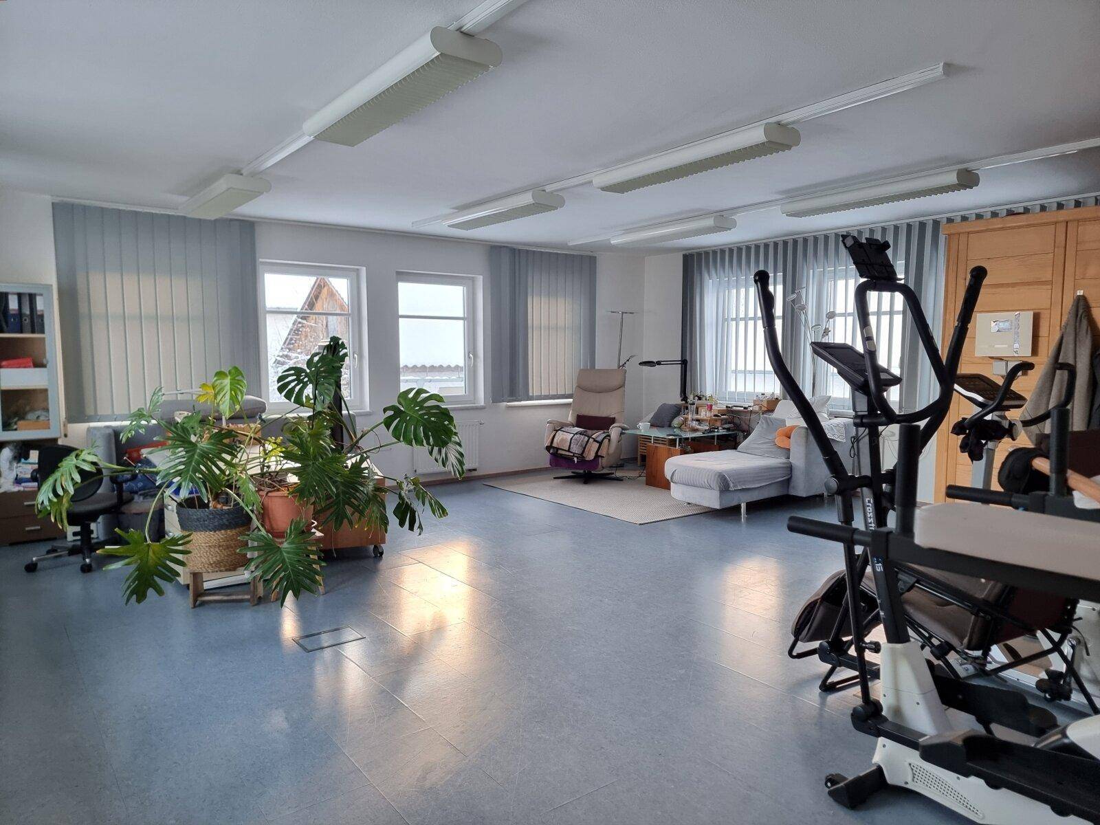Großzügiger Wohnraum mit Fitnessgeräten, Pflanzen und mehreren Fenstern.
