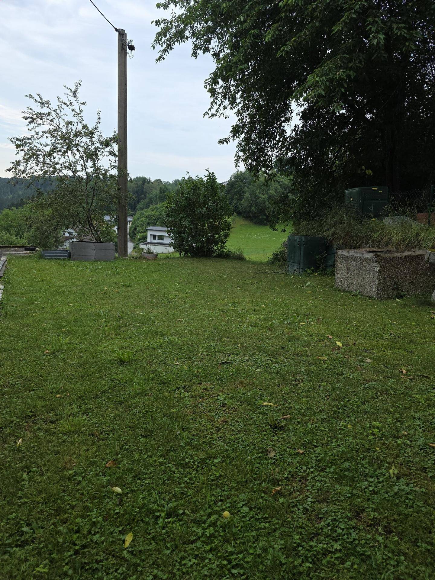 Großer Rasenbereich mit Bäumen und weitem Blick auf die umliegende Hügellandschaft und Häuser.