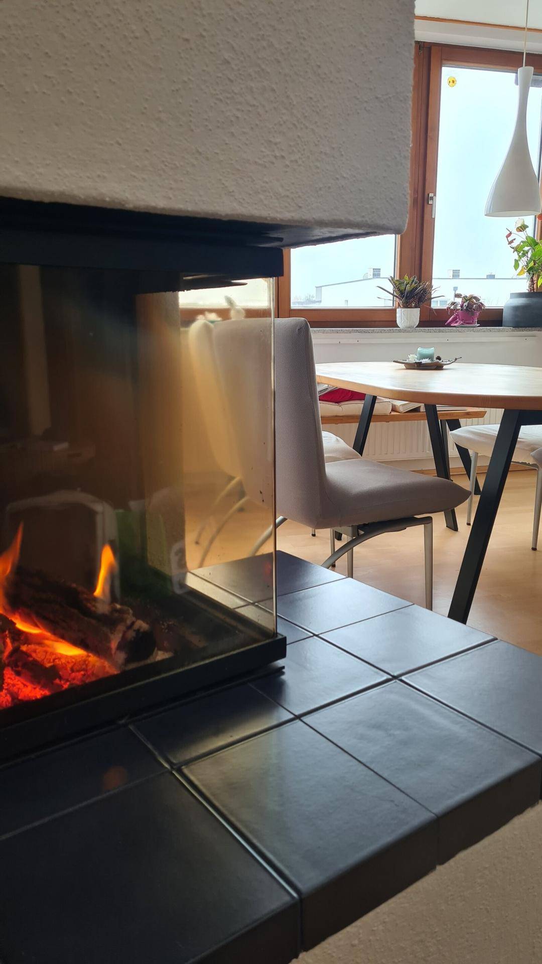 Detailaufnahme des modernen Kachelofens mit sichtbarem Feuer und dunklen Fliesen.