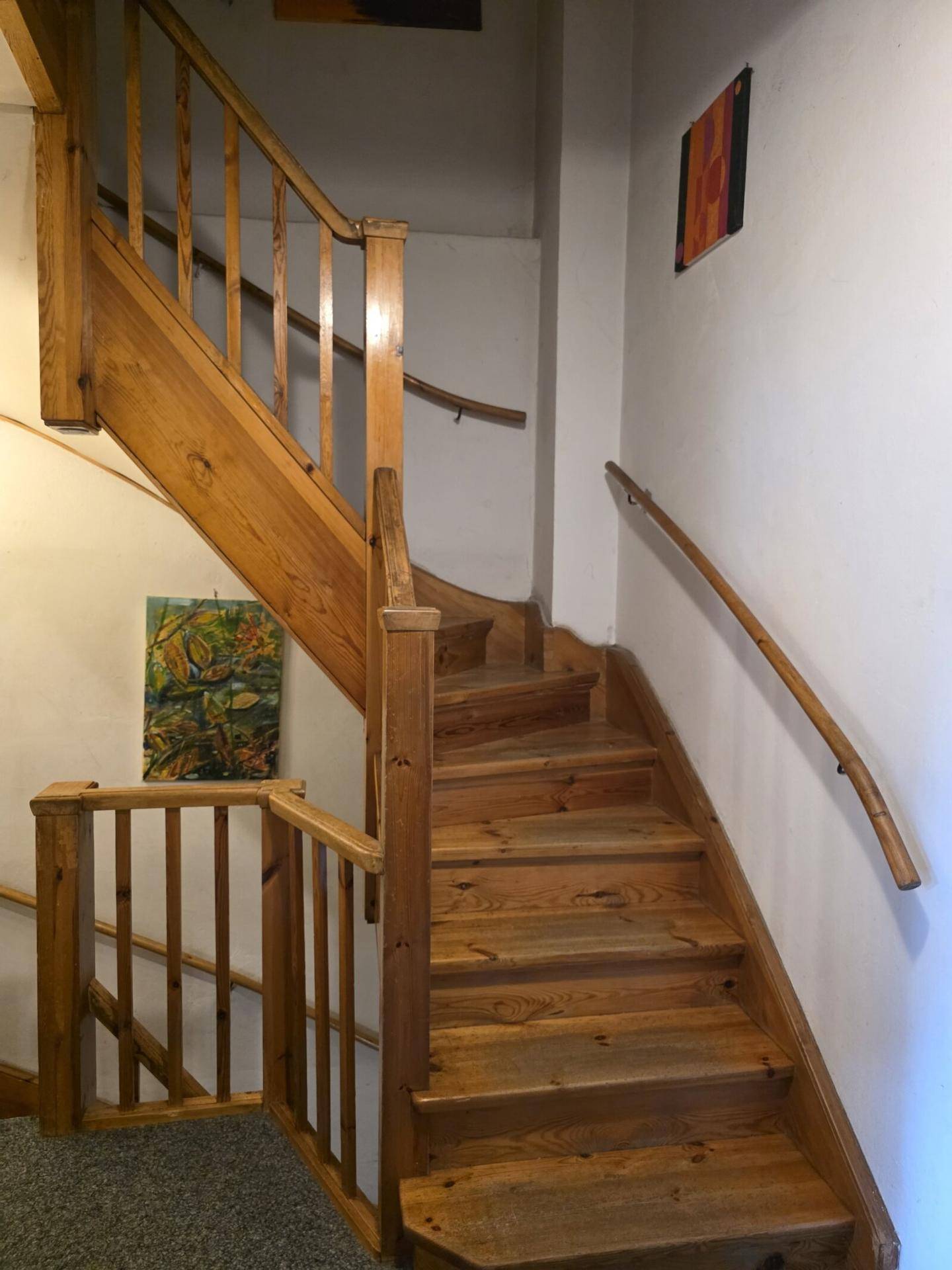Helle Holztreppe mit Geländer, die zu den oberen Stockwerken des Hauses führt.