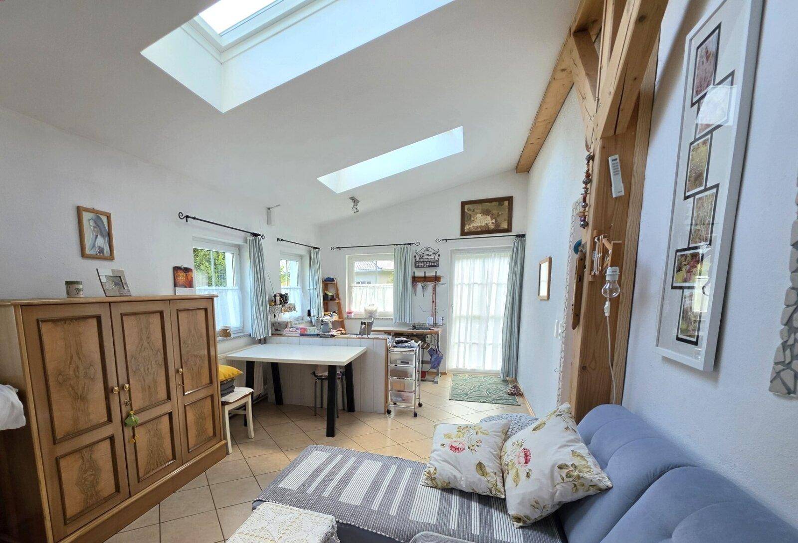 Heller Wohnraum mit Dachfenstern, sichtbaren Holzbalken und Zugang zu einem Balkon oder Terrasse.
