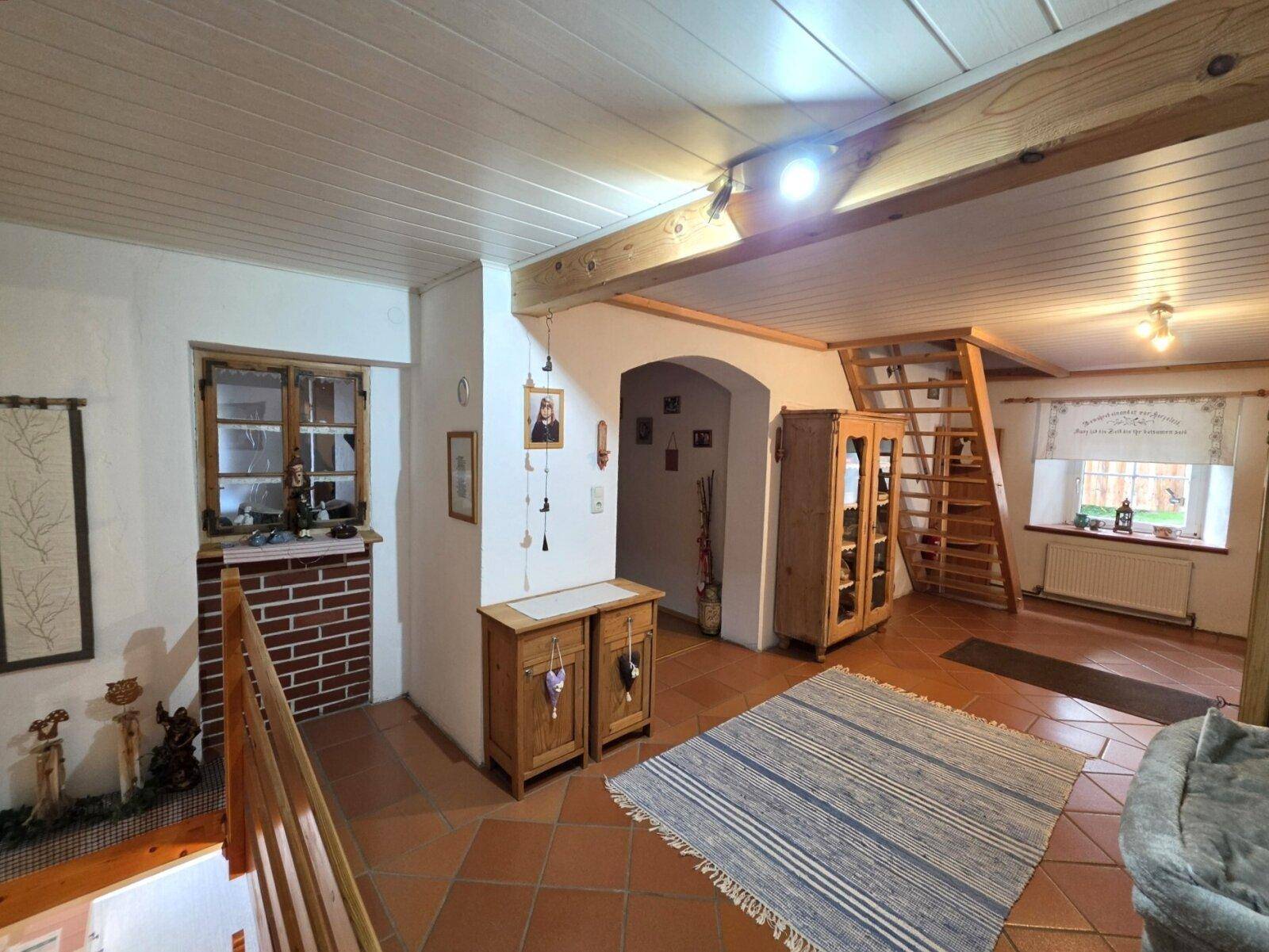 Heller Eingangsbereich mit Terrakottaboden, Holztreppe und sichtbaren Deckenbalken.
