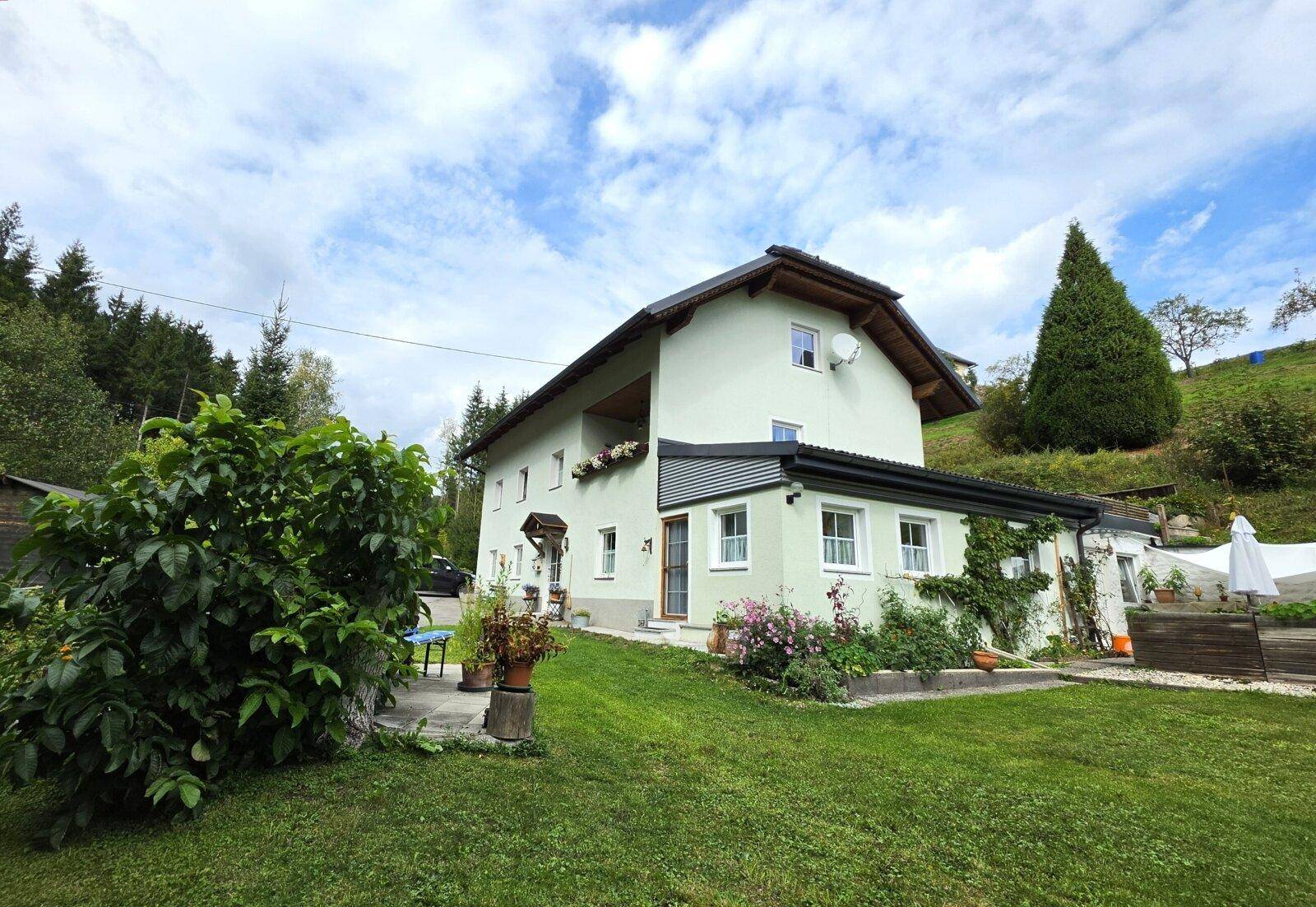 Seitenansicht des Hauses mit gepflegtem Garten und Blick auf die umliegende Natur.