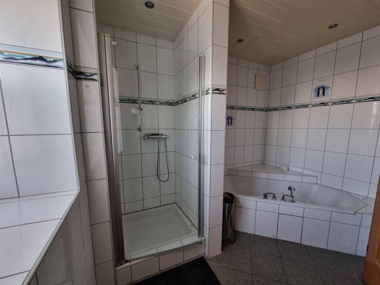 Badezimmer mit Duschkabine, Eckbadewanne und gefliesten Wänden.