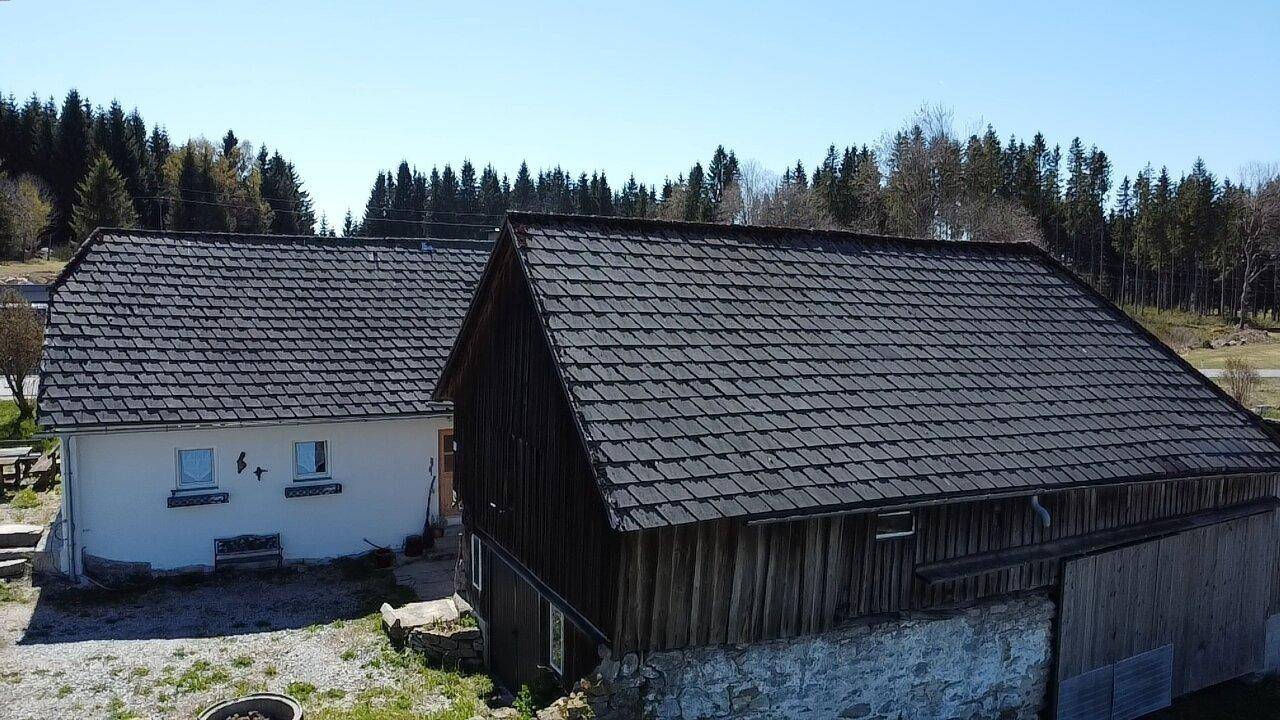 Nahaufnahme der Dächer des Hauses und der Scheune mit traditionellen Ziegeln und Holzfassade.
