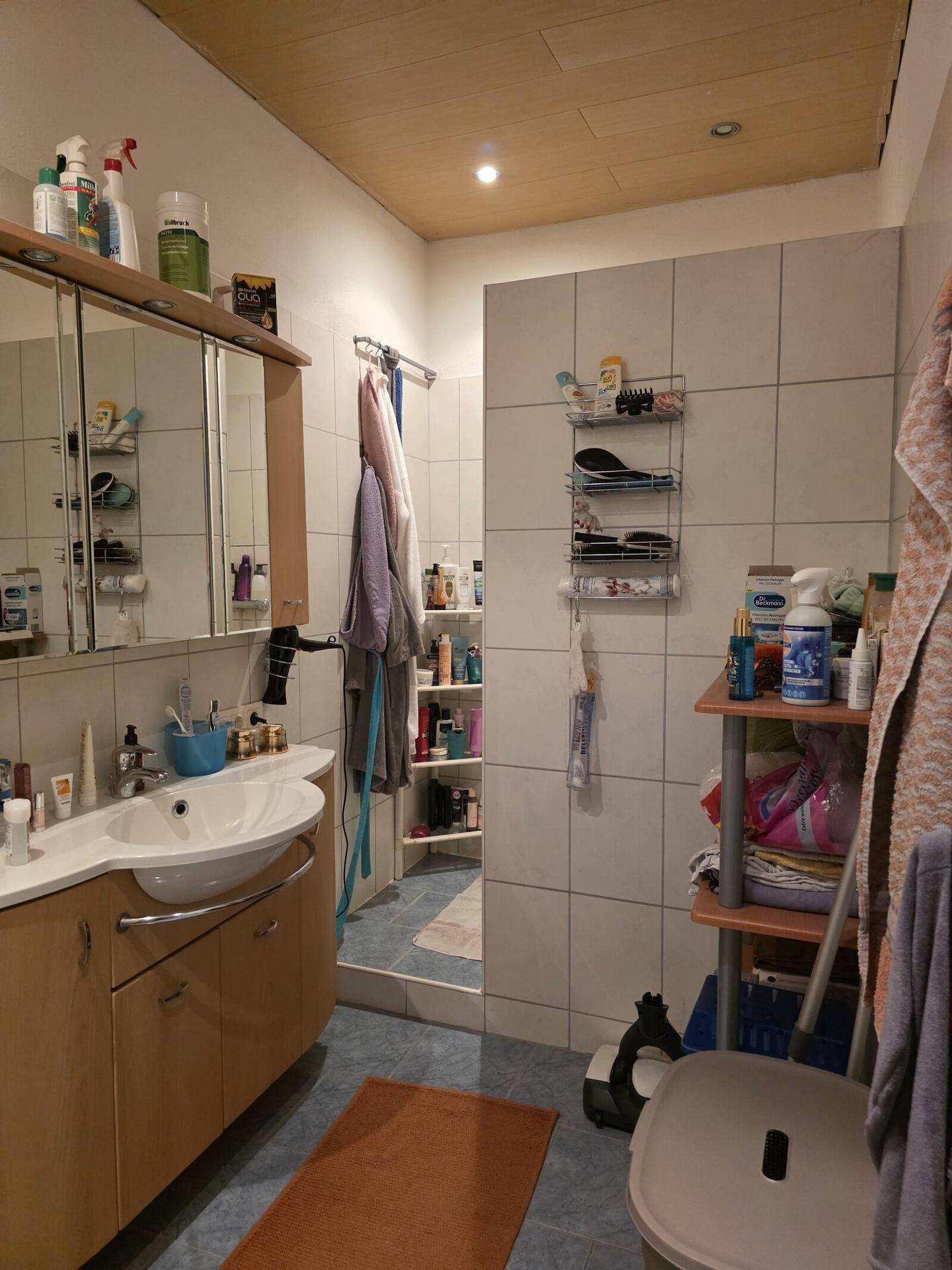 Badezimmer mit Waschbecken, Spiegelschrank und Duschbereich, komplett gefliest.