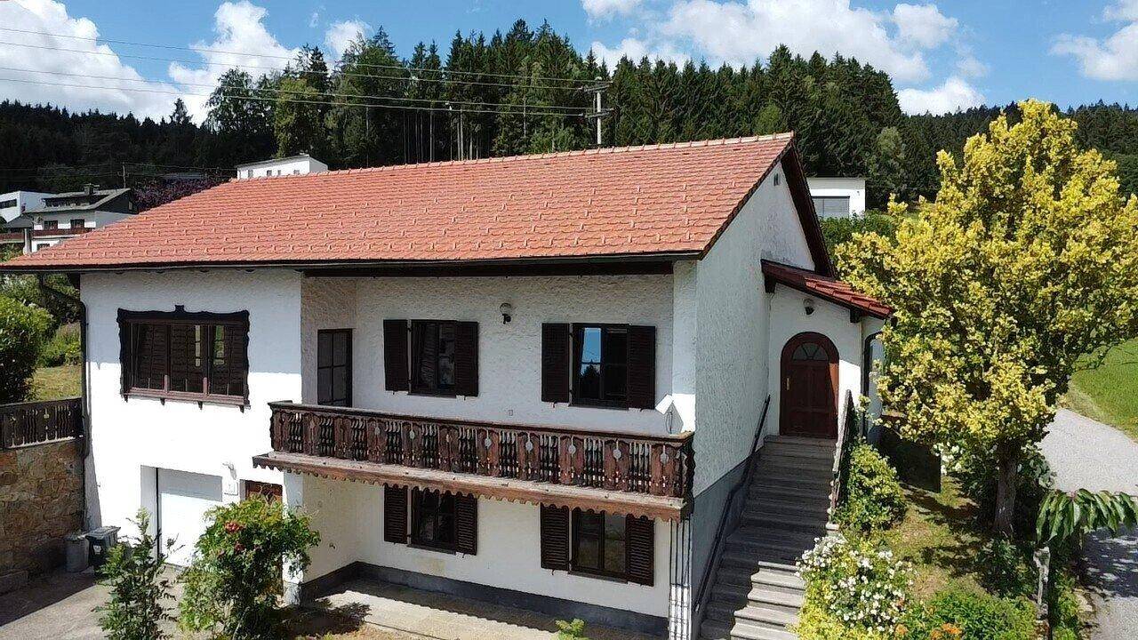 Vorderansicht des Einfamilienhauses mit Balkon, Holzfensterläden und Zugang über eine Außentreppe.